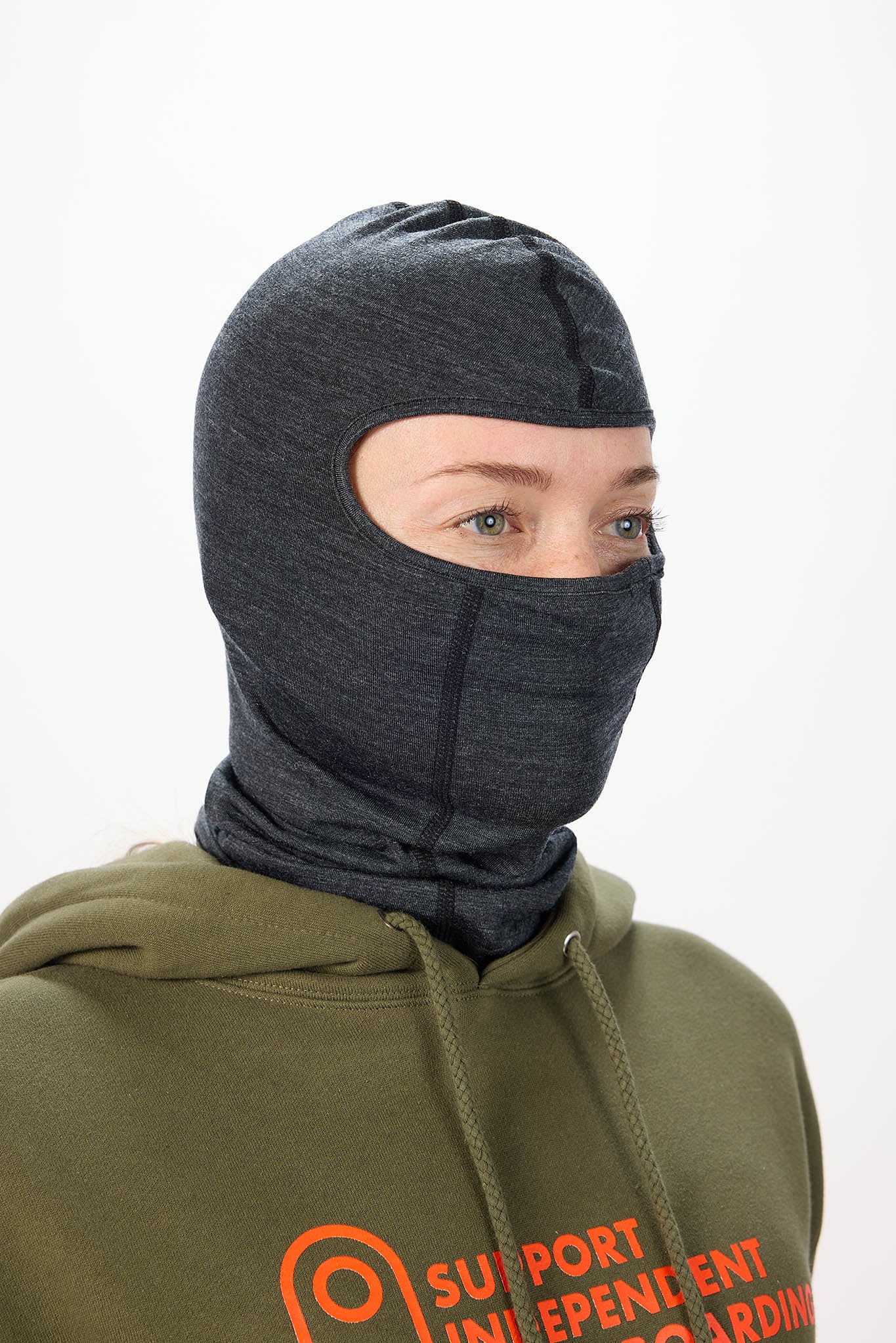 A person wearing a dark heather gray full-head balaclava mask over an olive green hoodie with orange text on the front, photographed against a plain light background.