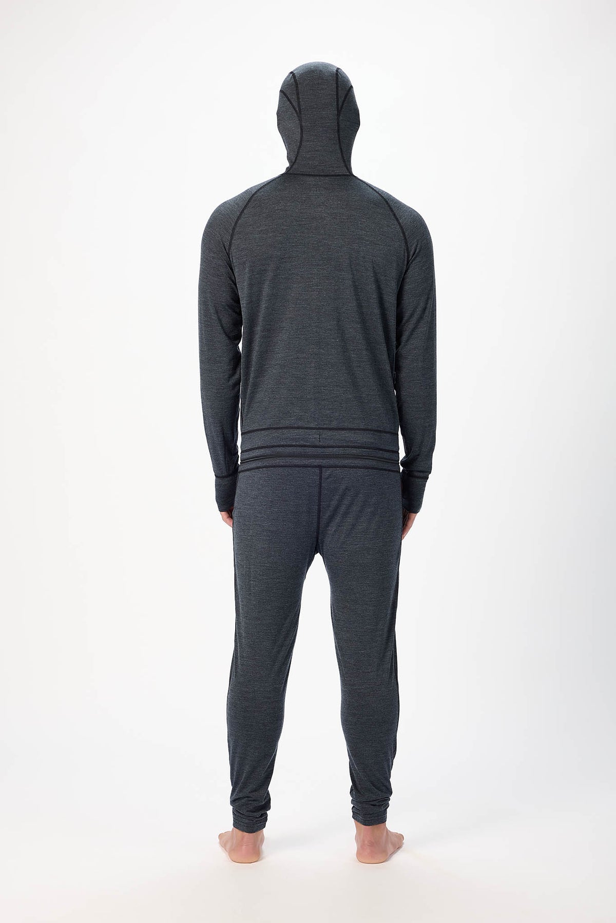 view from behind A man wearing a black hooded zip-up onesie , standing barefoot against a plain white studio background.
