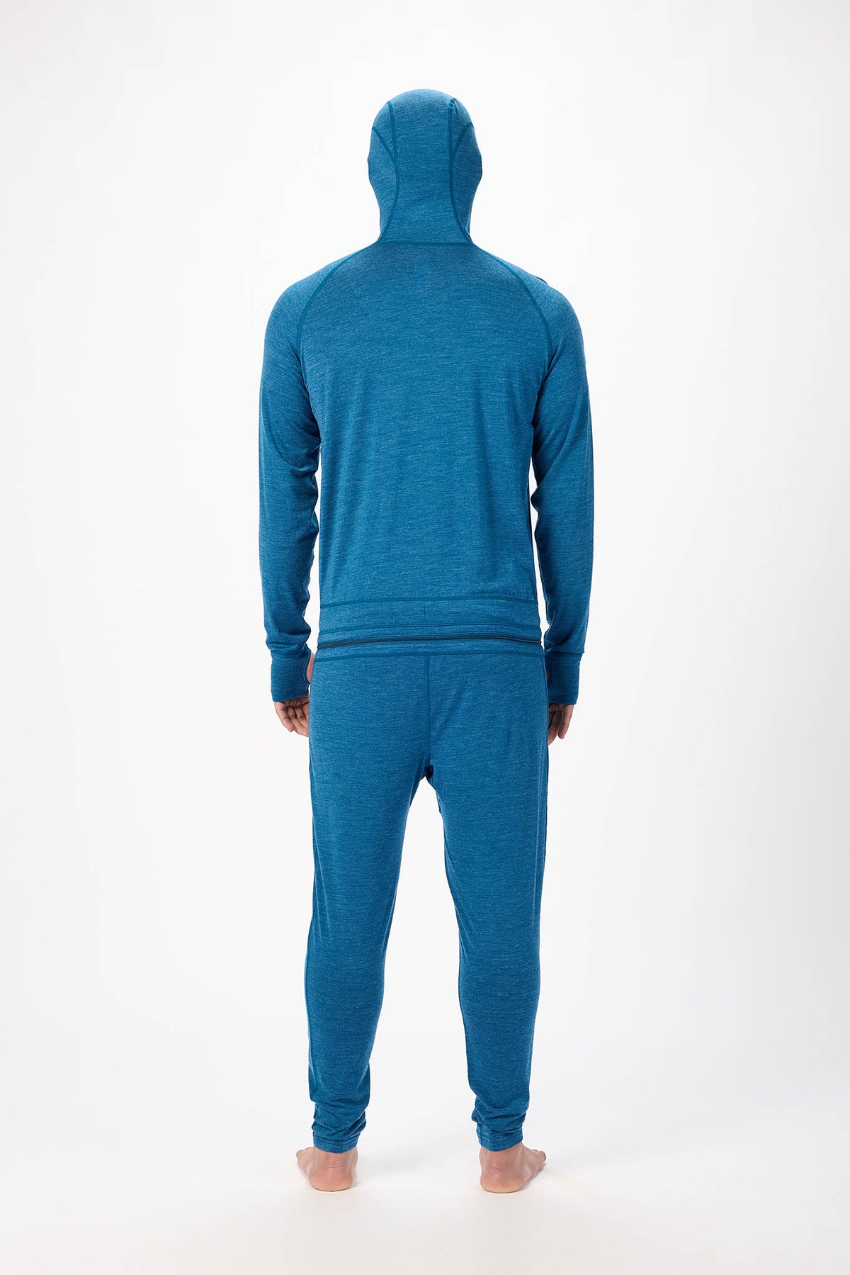 view from behind A man wearing a blue hooded zip-up onesie , standing barefoot against a plain white studio background.