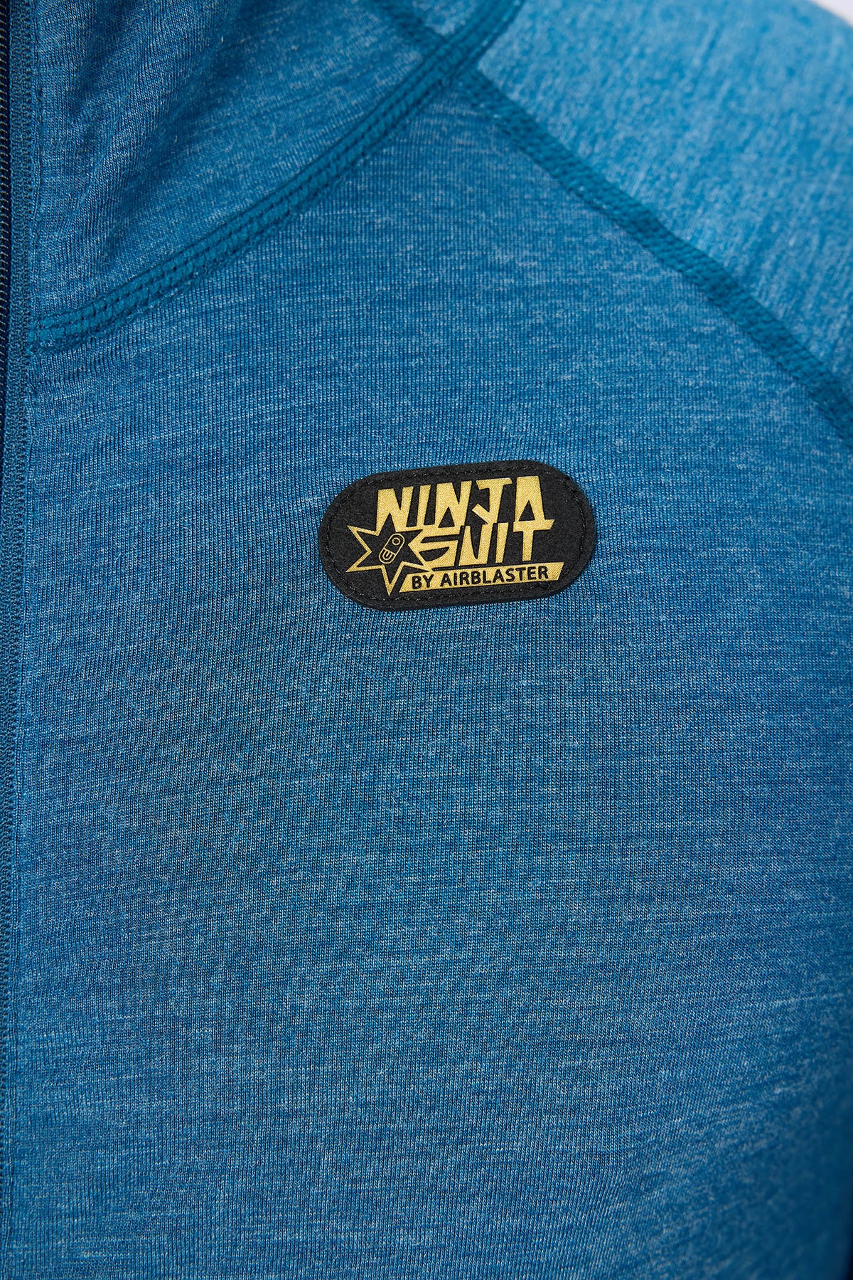 Close-up of a blue heathered athletic jacket with a black oval patch on the chest that reads 'NINJA SUIT' and 'BY AIRBLASTER'.