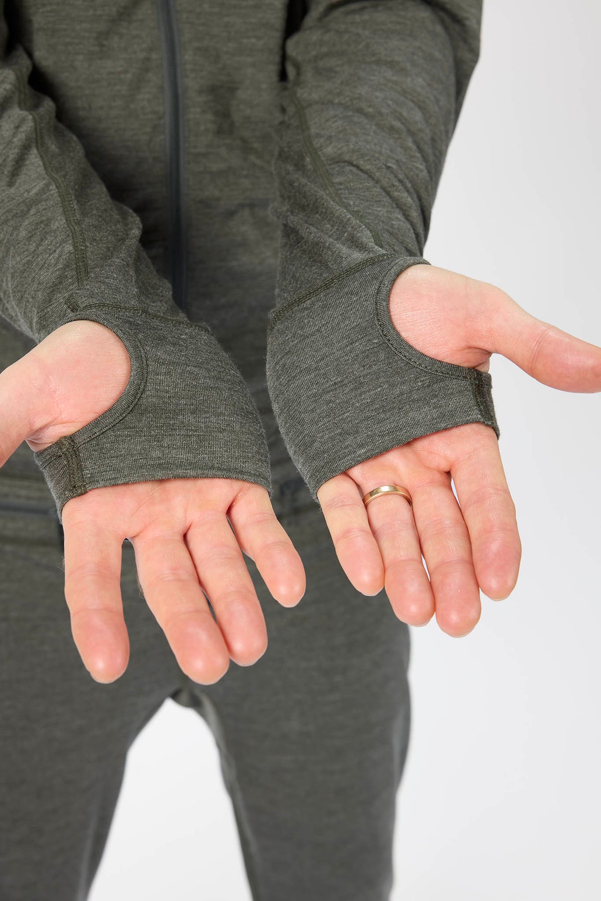 Close-up of a person wearing a dark heather gray athletic zip-up hoodie with thumbholes, showing the fit on their hands against a light gray background.