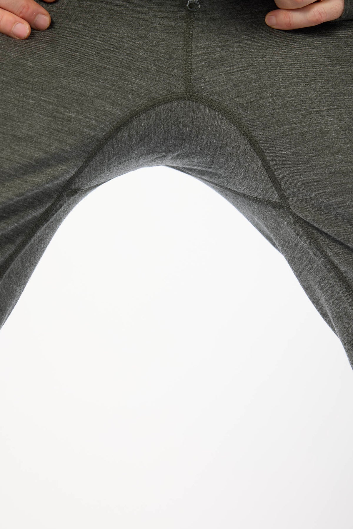 Close-up of dark gray heathered athletic leggings being pulled outward by hands to show the stretch and seam construction, against a white background.