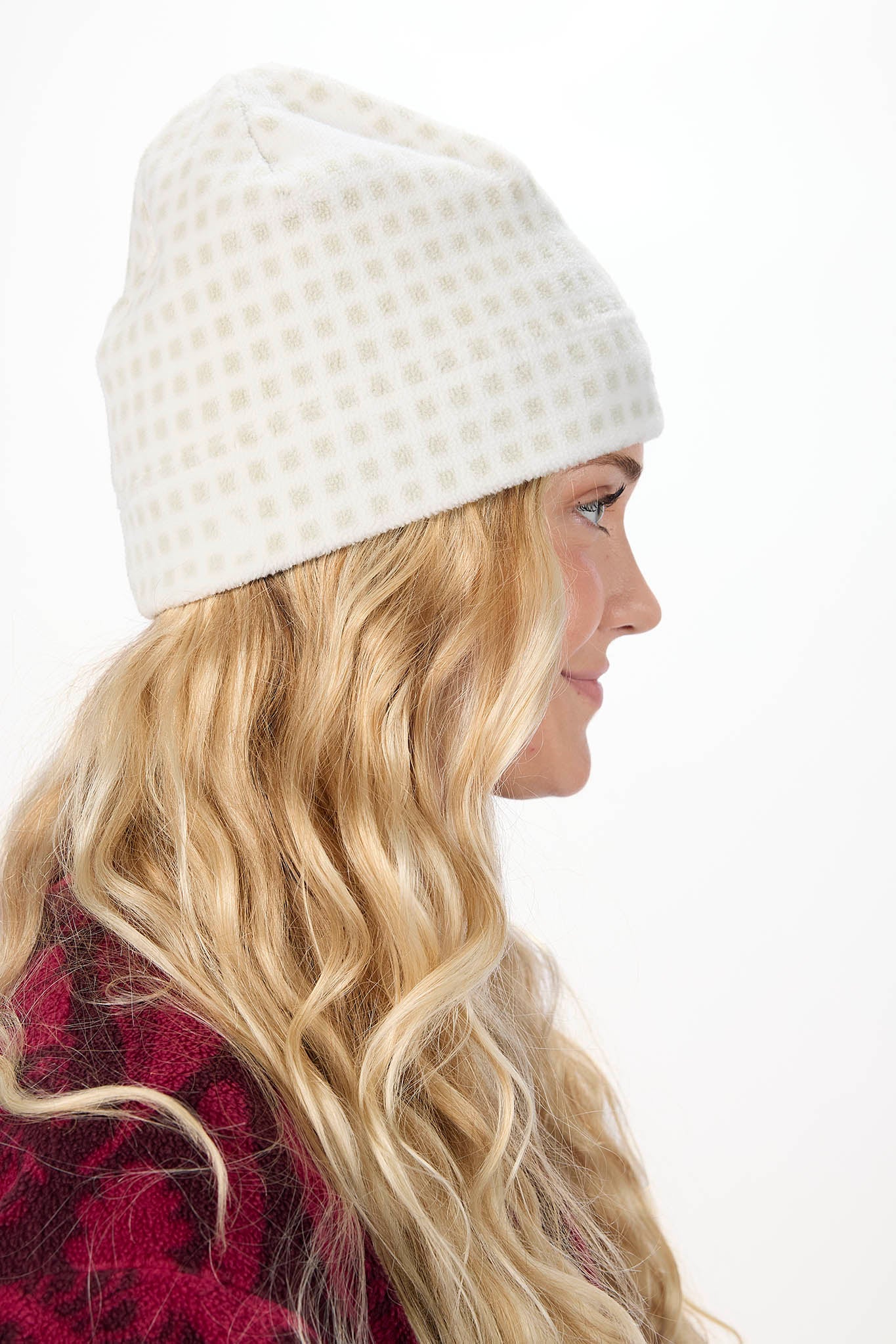 A woman in profile wearing a cream-colored beanie with a subtle grid pattern, set against a plain white background.