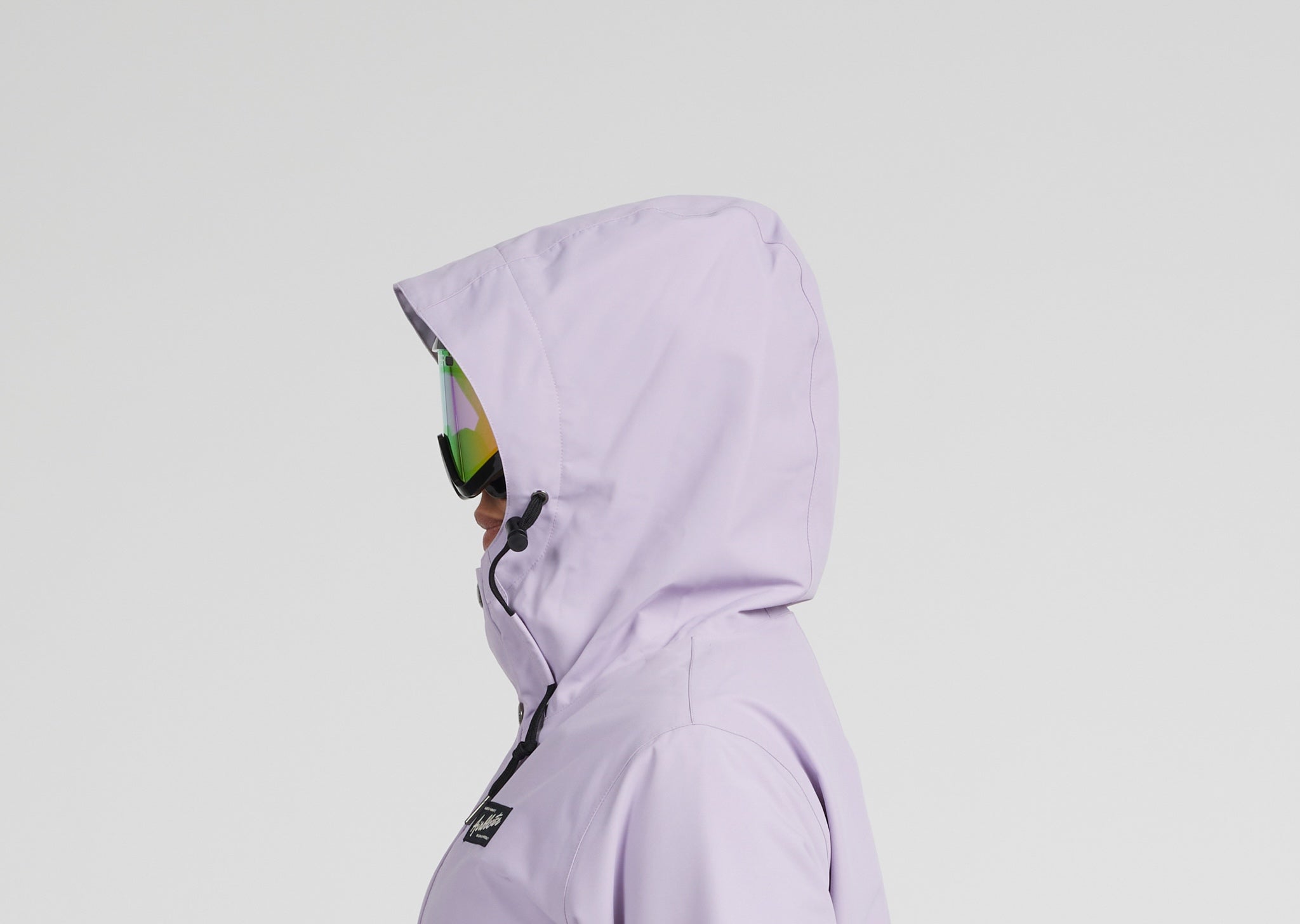 A side profile of a person wearing a light lavender hooded jacket and reflective green-tinted goggles, set against a solid light gray background.