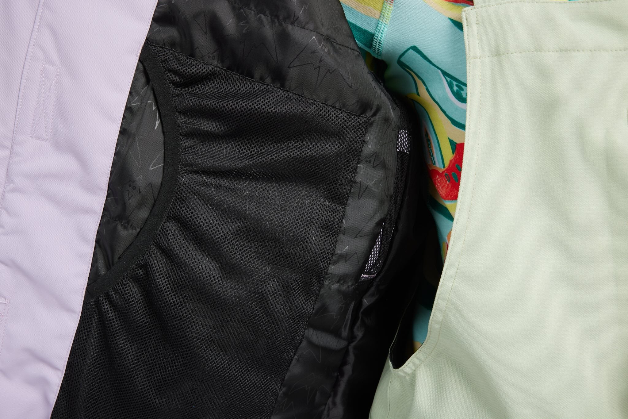 Close-up detail of a jacket showing a black mesh pocket, a light lavender outer section, and a mint green section with a colorful patterned lining.