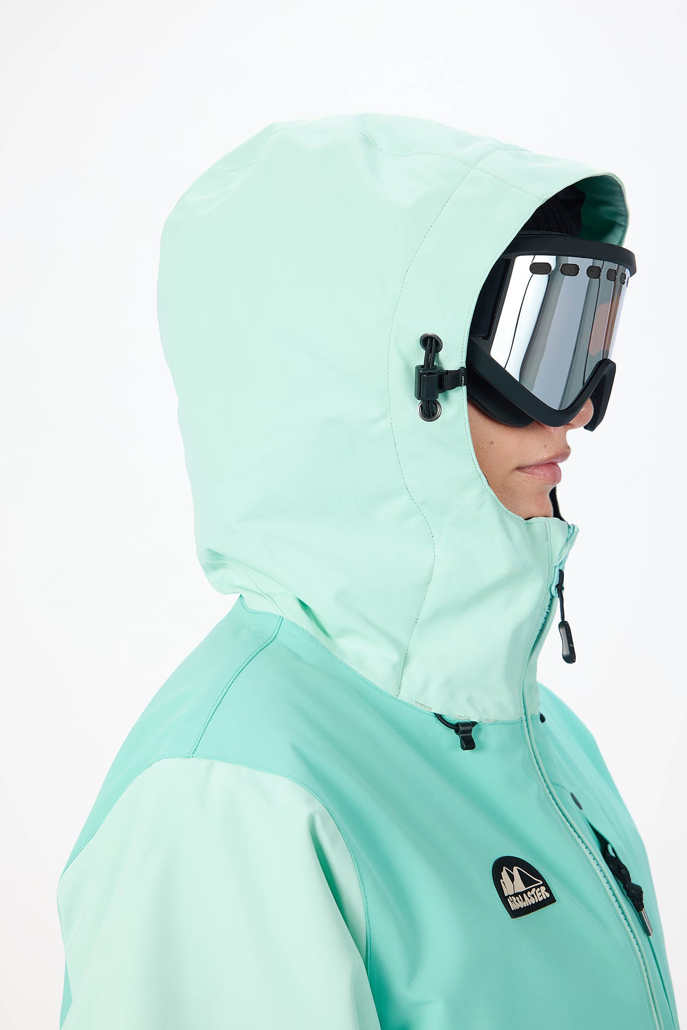 Person wearing a light green snow jacket and goggles on a white background