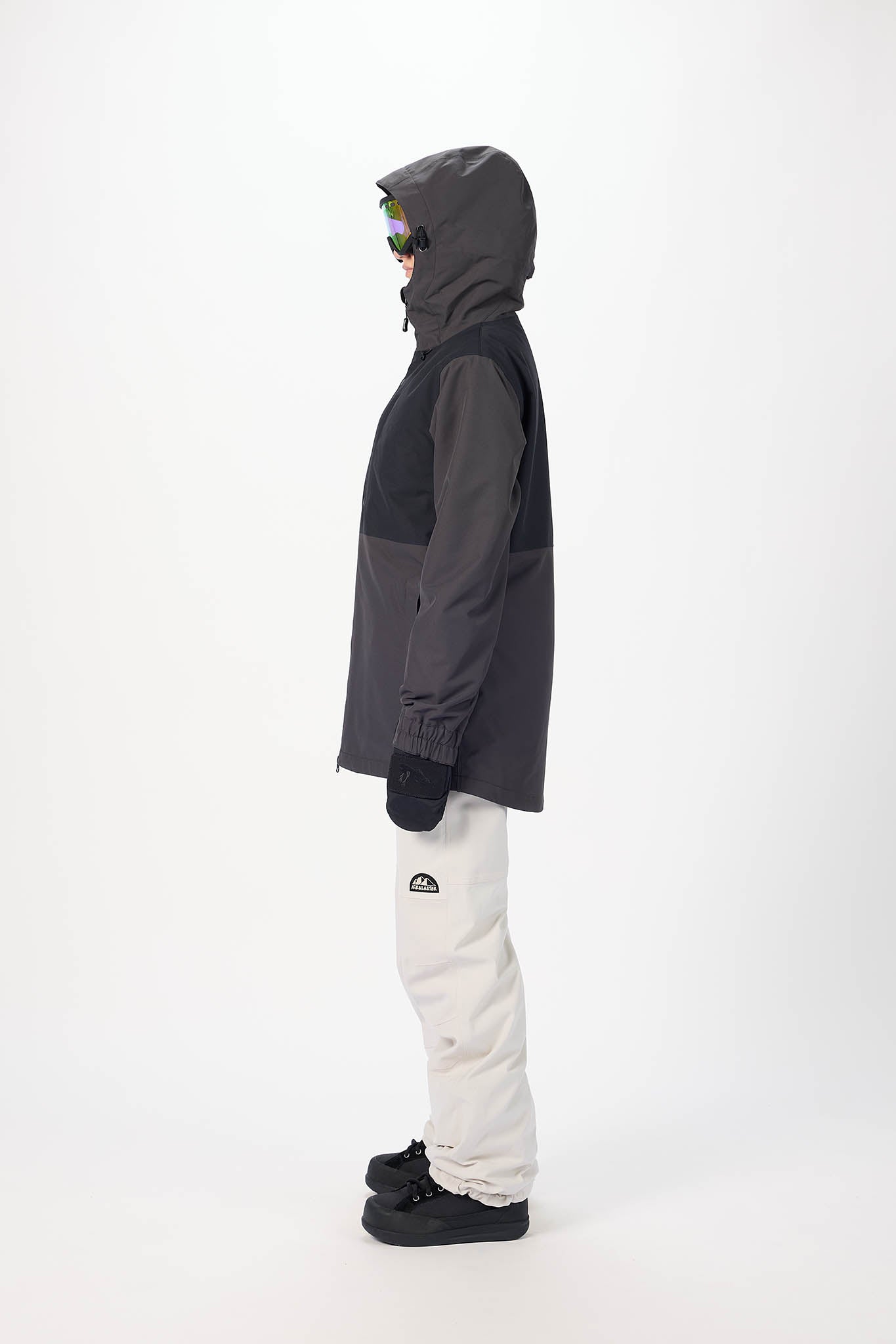 Person wearing a dark gray and black jacket with a hood, white pants, and black shoes on a white background