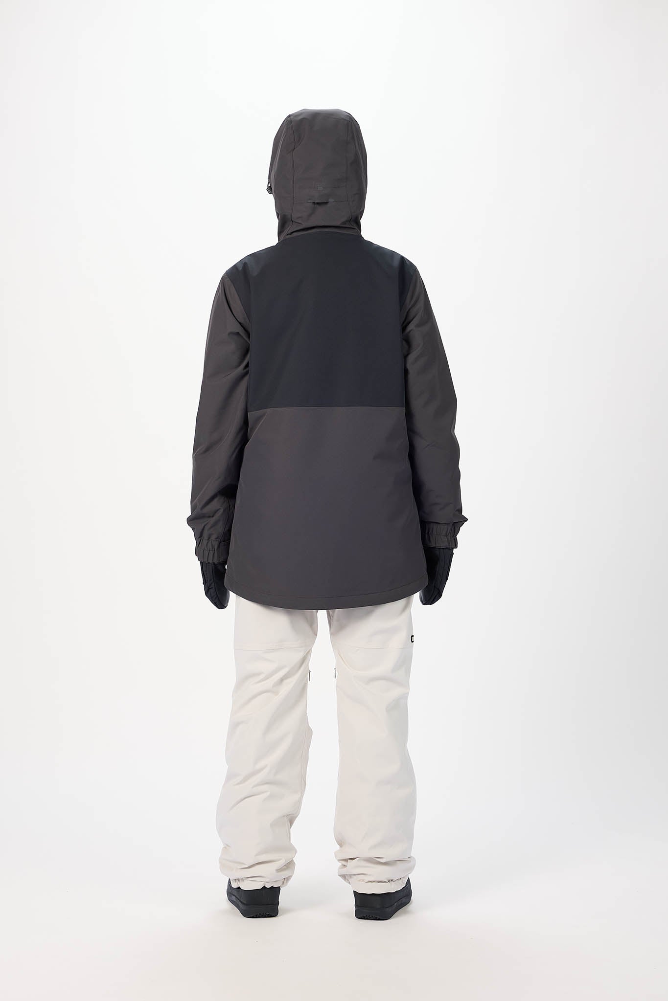 Person wearing a black and gray jacket with white pants on a white background