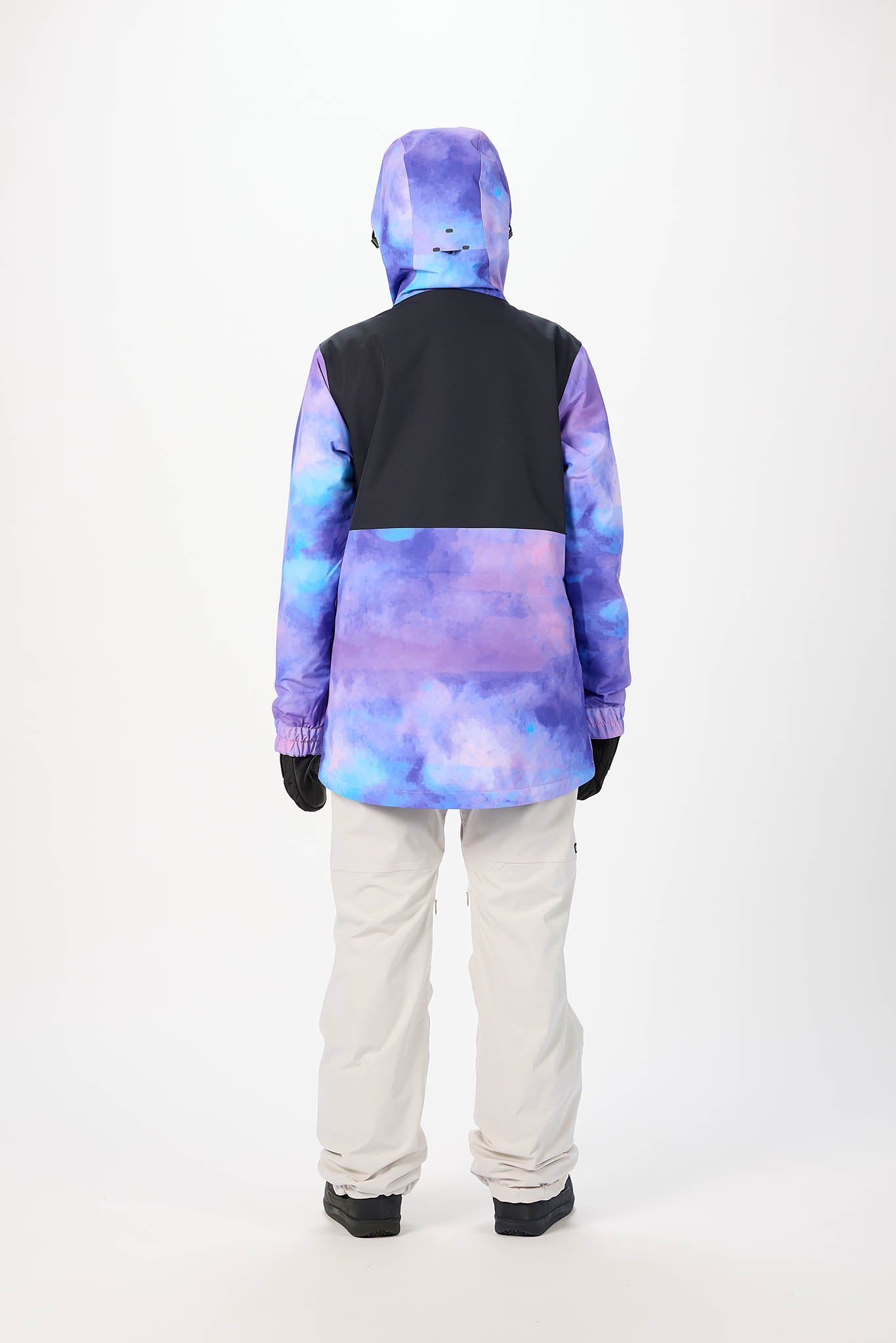Person wearing a colorful jacket with a black vest and white pants on a white background