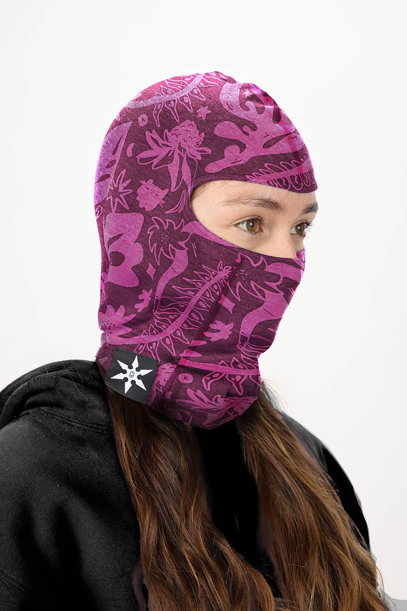 A person wearing a plum earth print balaclava face mask over an olive green hoodie, shown against a plain white background.