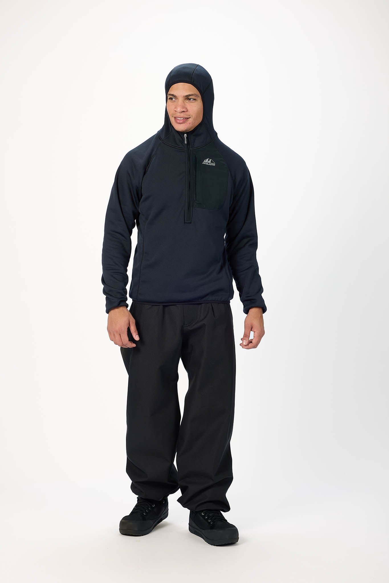 A man modeling a dark navy quarter-zip hooded jacket and black pants against a plain white studio background.