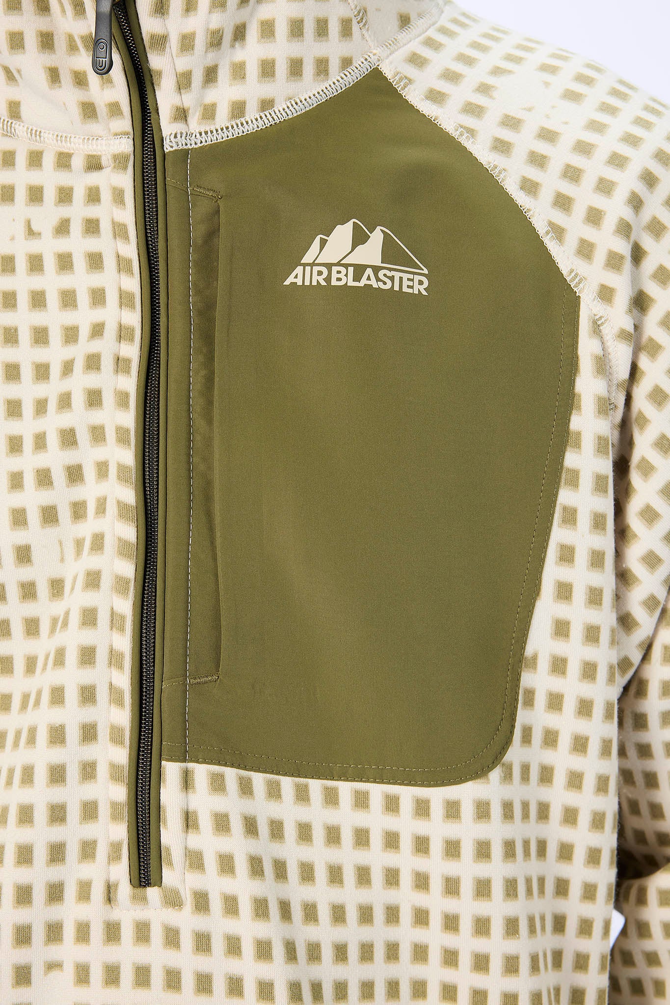 Close-up of a quarter-zip pullover jacket with an olive green chest panel and white 'AIR BLASTER' logo, paired with a beige and white checkered patterned body.