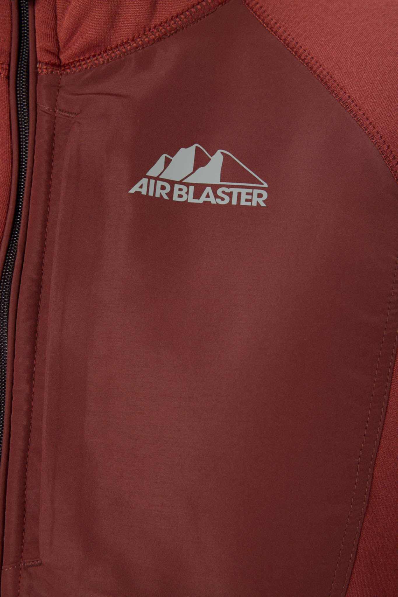 Close-up of a rust-red zippered jacket with a white 'AIR BLASTER' mountain logo on the chest.