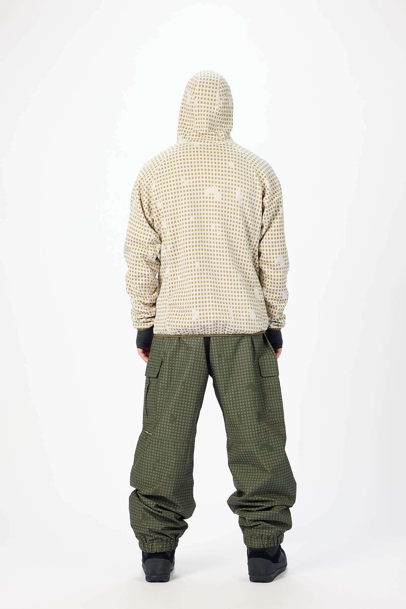 A person shown from the back wearing a beige and white checkered hooded jacket and olive green checkered pants, standing against a plain white studio background.