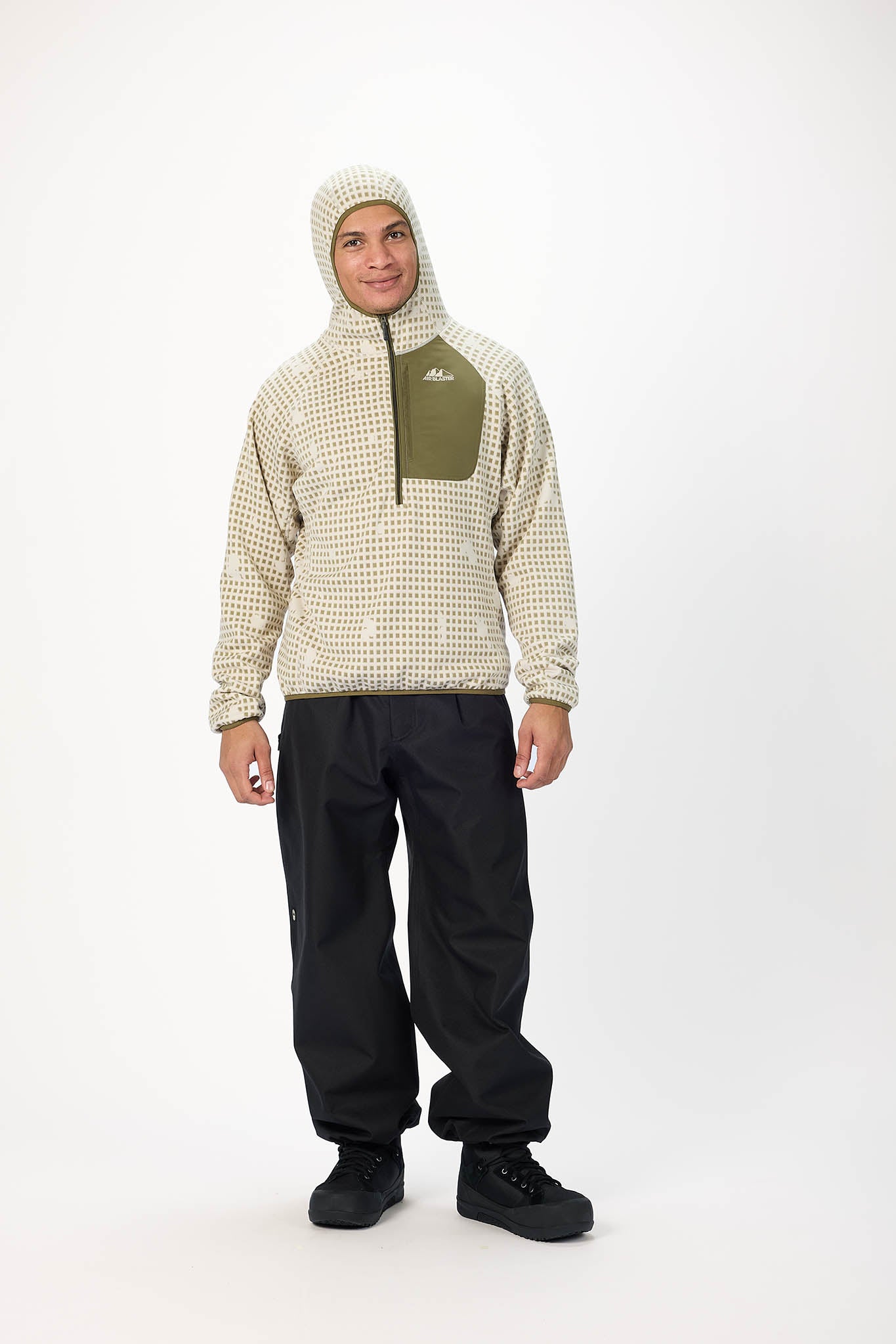A man modeling a beige and white patterned fleece jacket with an olive green chest pocket, a matching knit beanie, and black snow pants against a white studio background.