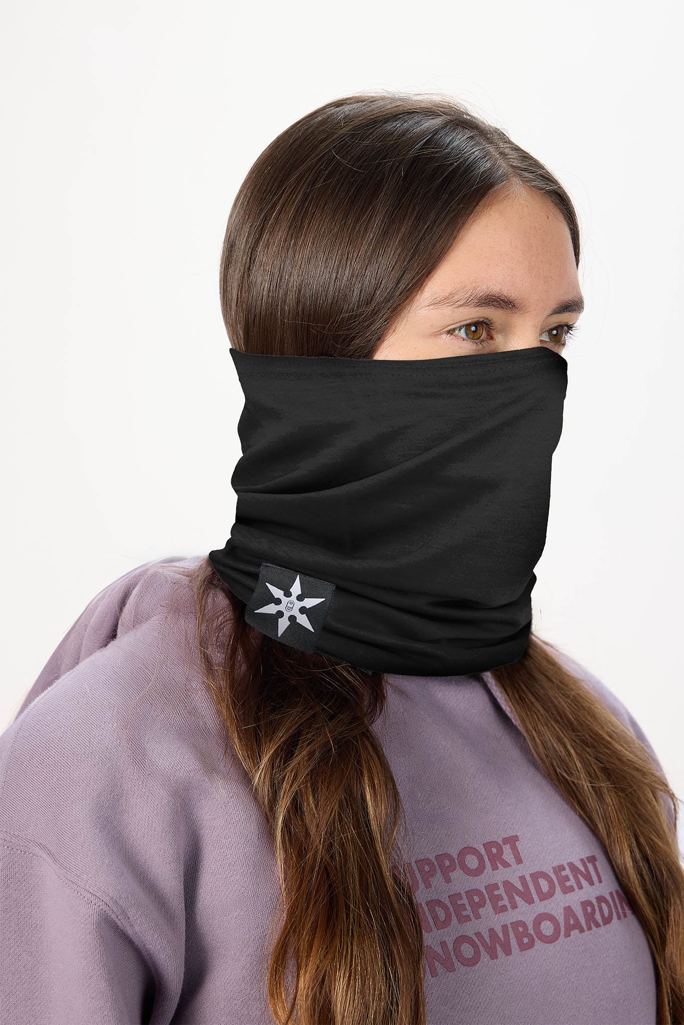 A woman wearing a black neck gaiter with a white snowflake logo, paired with a lavender hoodie against a plain white background.