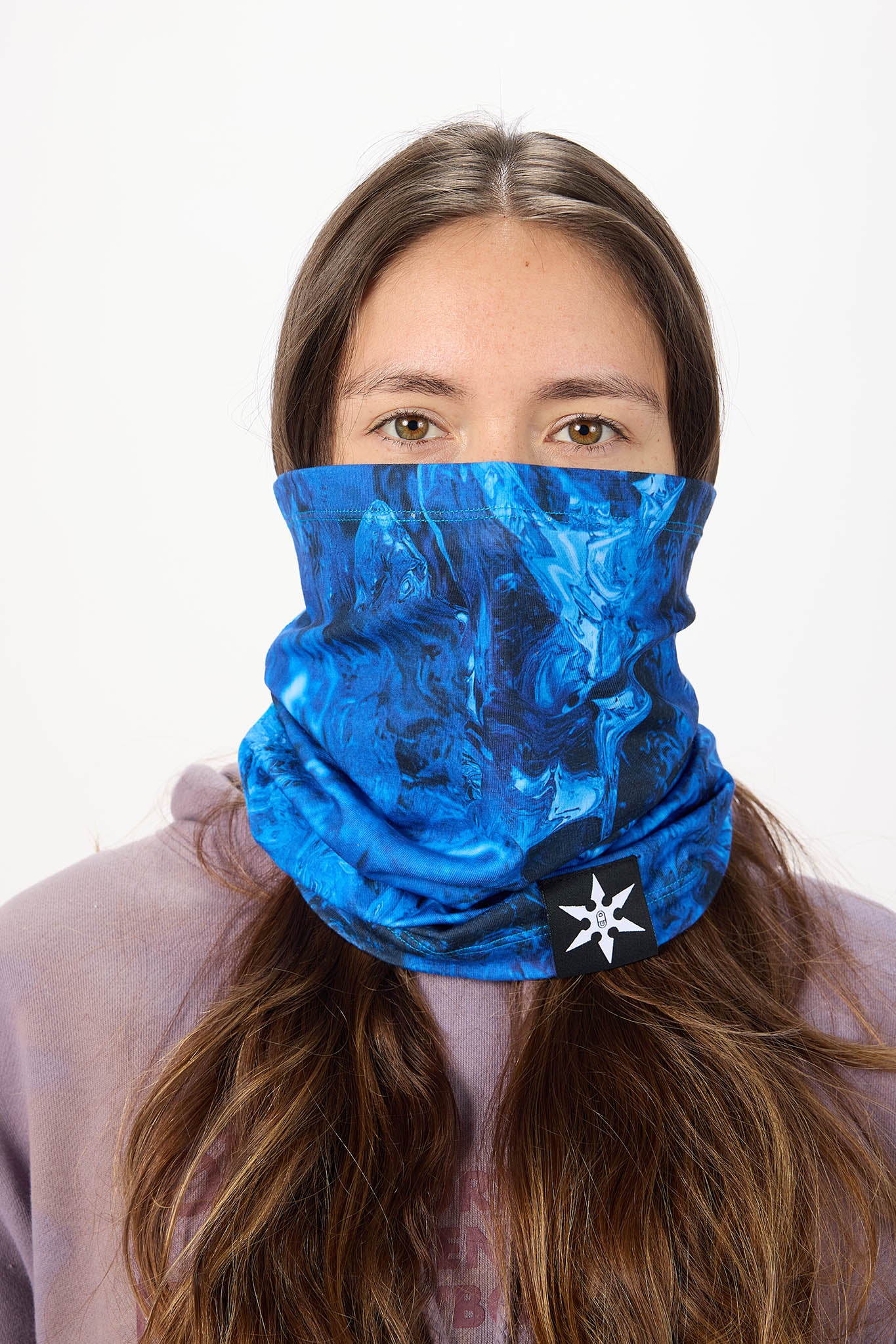 A woman wearing a blue marbled patterned neck gaiter mask with a white star logo, shown against a plain white background.
