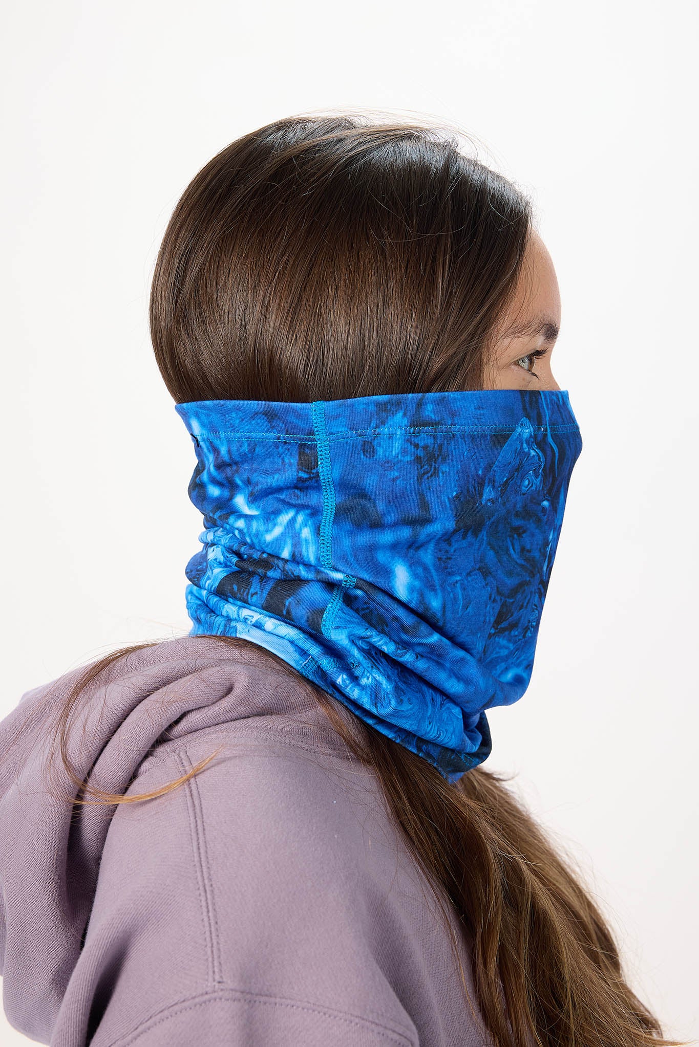 A person shown from the side wearing a blue patterned neck gaiter or face covering around the lower face and neck, against a plain light background.