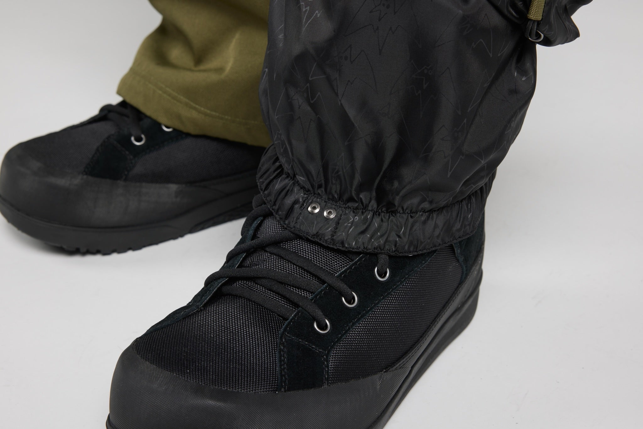 Black waterproof snowboard boots with laces and a black gaiter, shown on a person's feet against a light gray background.
