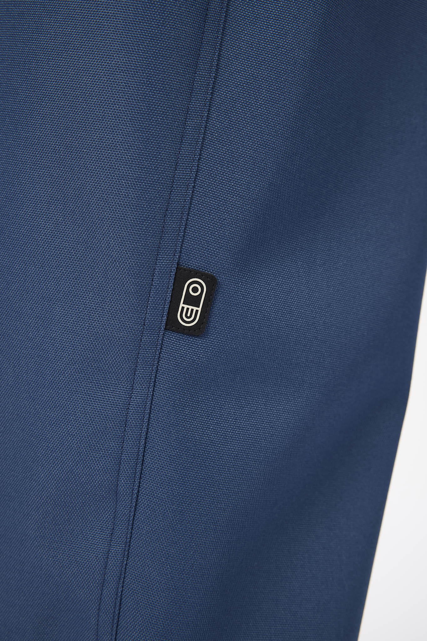 Close-up of a textured navy blue fabric with a small black rectangular brand patch featuring a white stylized 'm' logo.