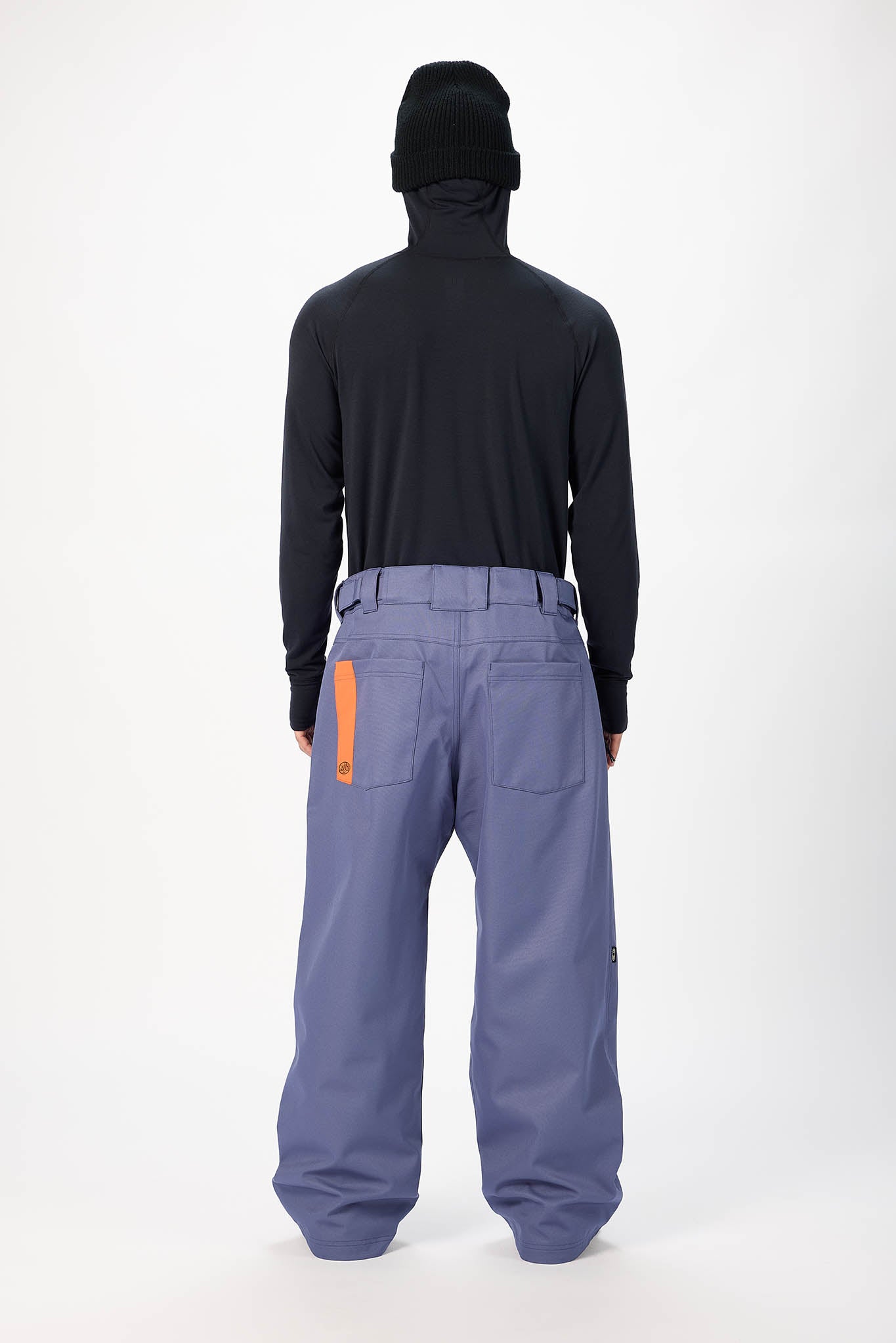 A model shown from the back wearing a black long-sleeve hooded top and wide-leg slate blue snow pants with an orange accent tab on the back pocket, against a plain white studio background.