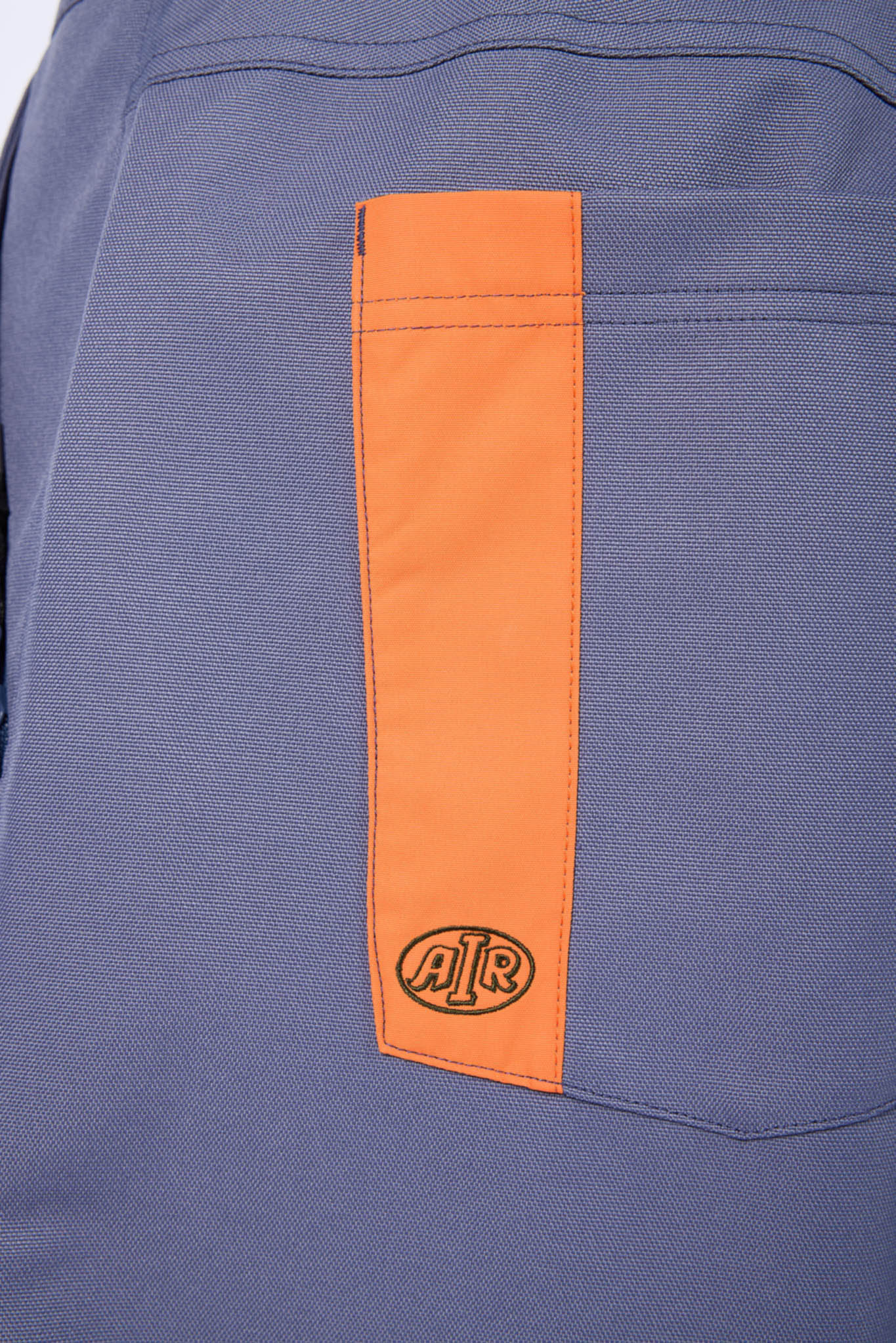 Close-up of a blue-gray fabric garment featuring a vertical orange pocket panel with an embossed circular 'AIR' logo near the bottom.