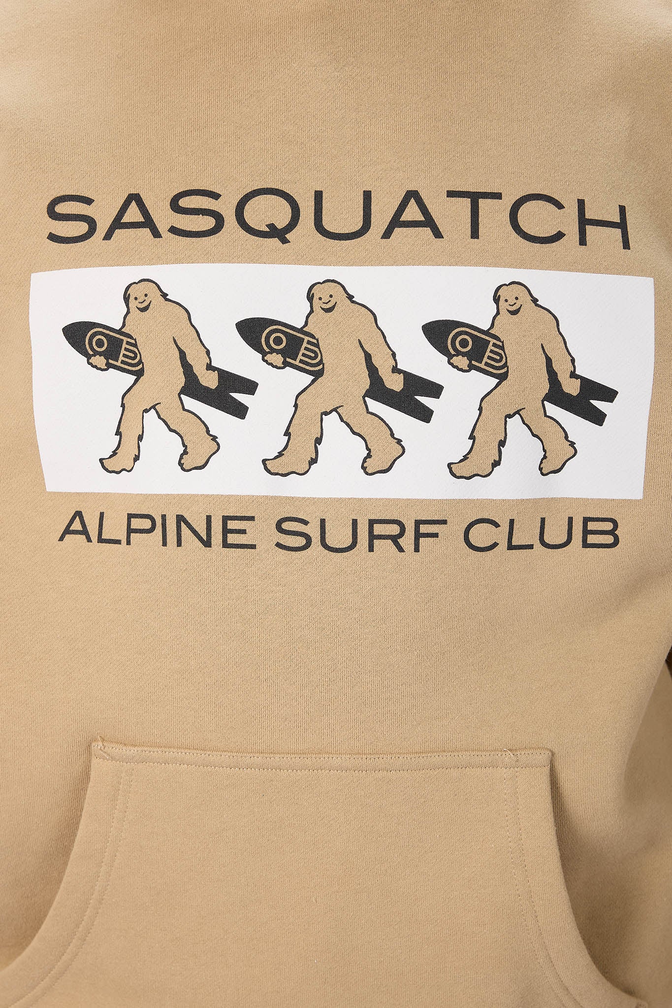 Close-up of a beige hoodie featuring a graphic print with the text 'SASQUATCH' and 'ALPINE SURF CLUB' and three cartoon sasquatch figures carrying surfboards on a white rectangular background.