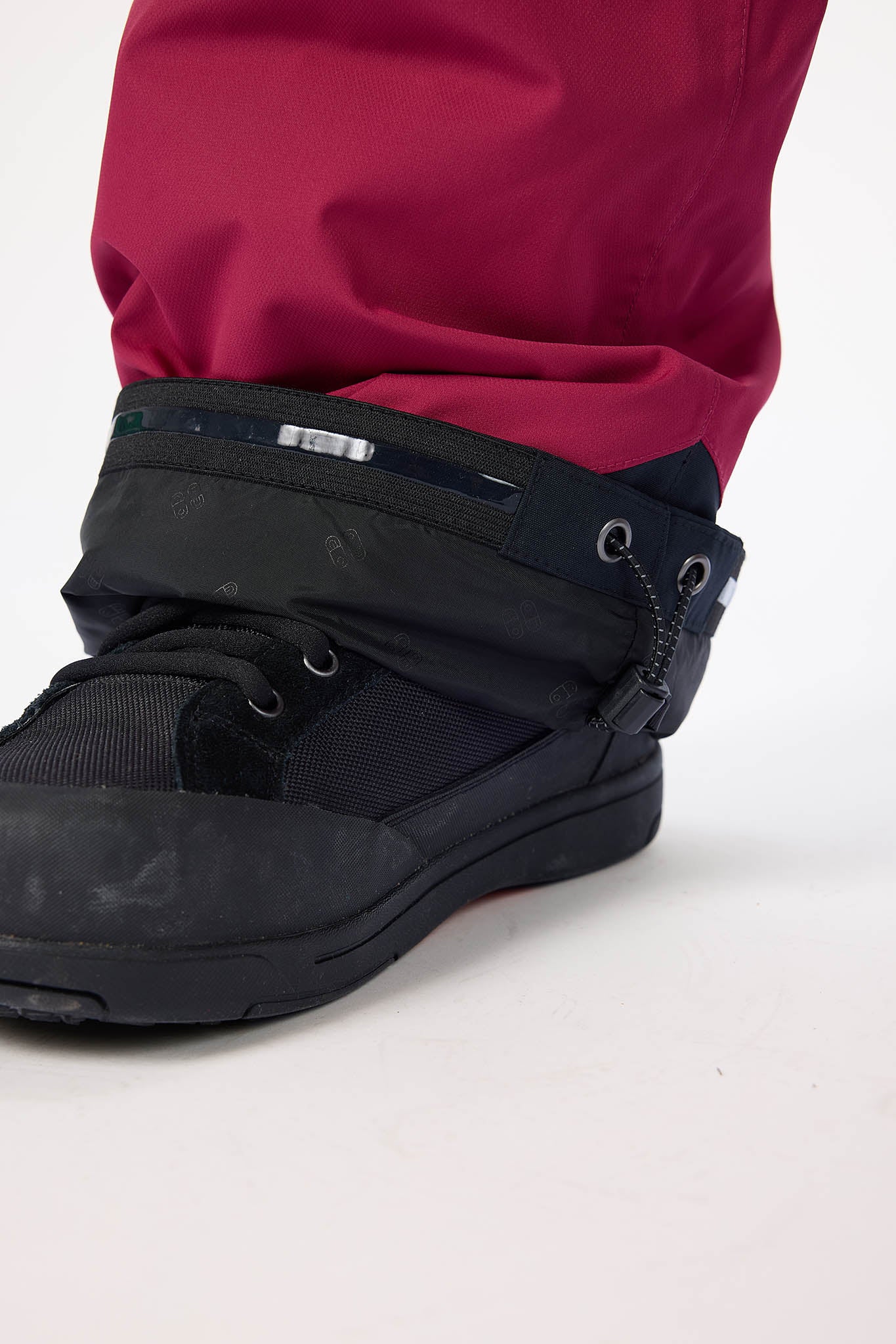 Black boot with a strap over a red pants leg on a white background