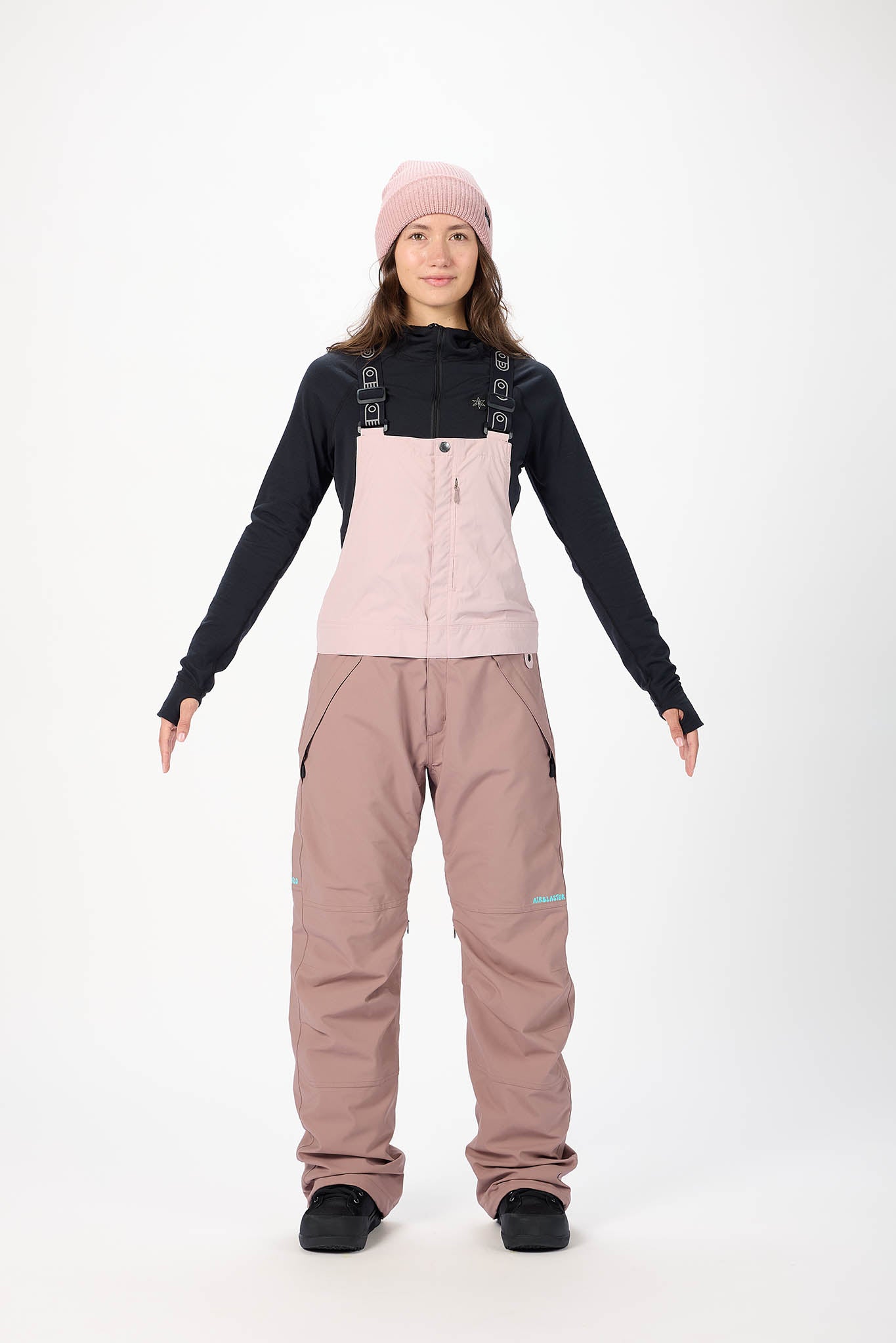 Person wearing a black jacket, pink bib overalls, and beige pants on a white background