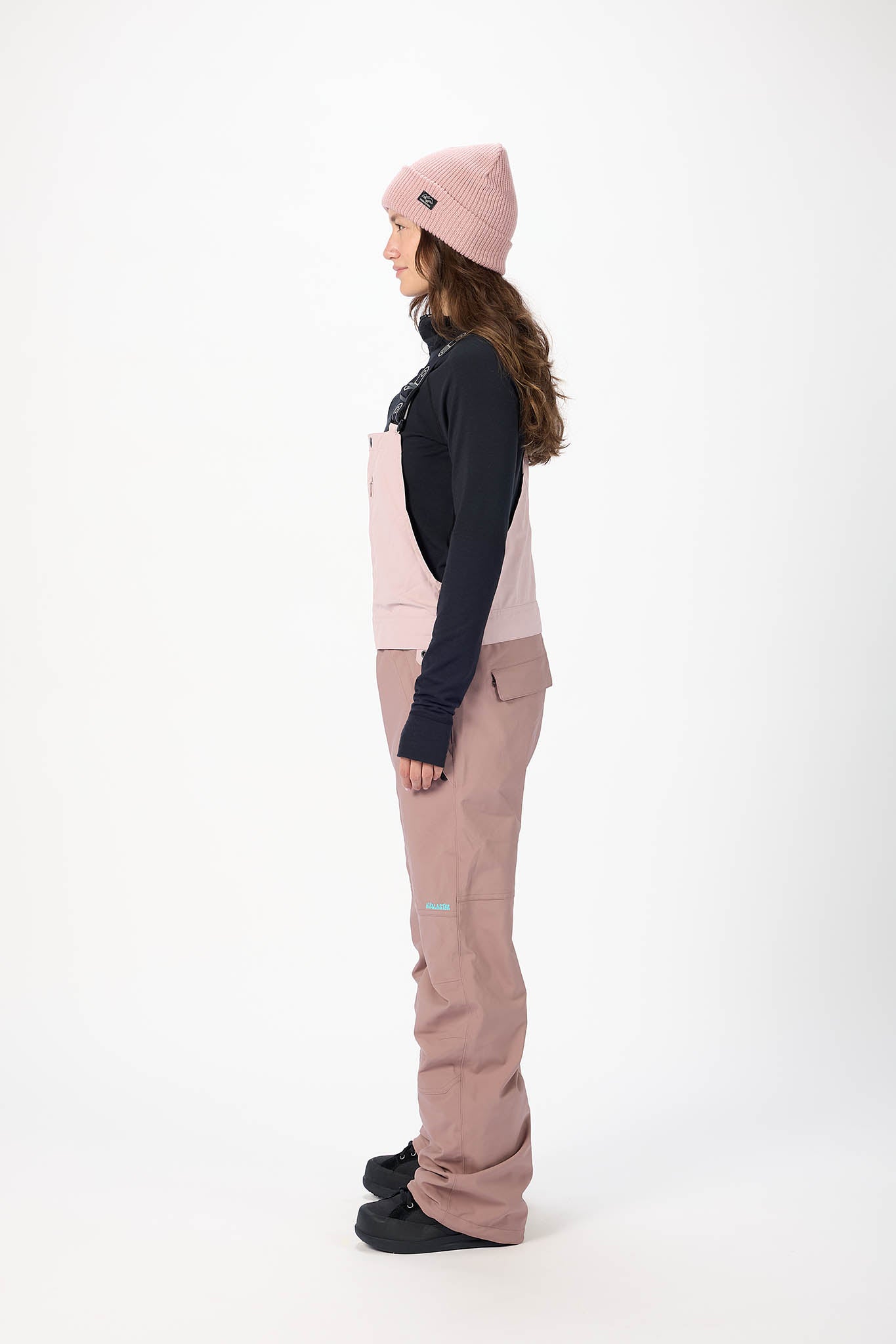 Person wearing a pink jacket, black shirt, and beige pants on a white background