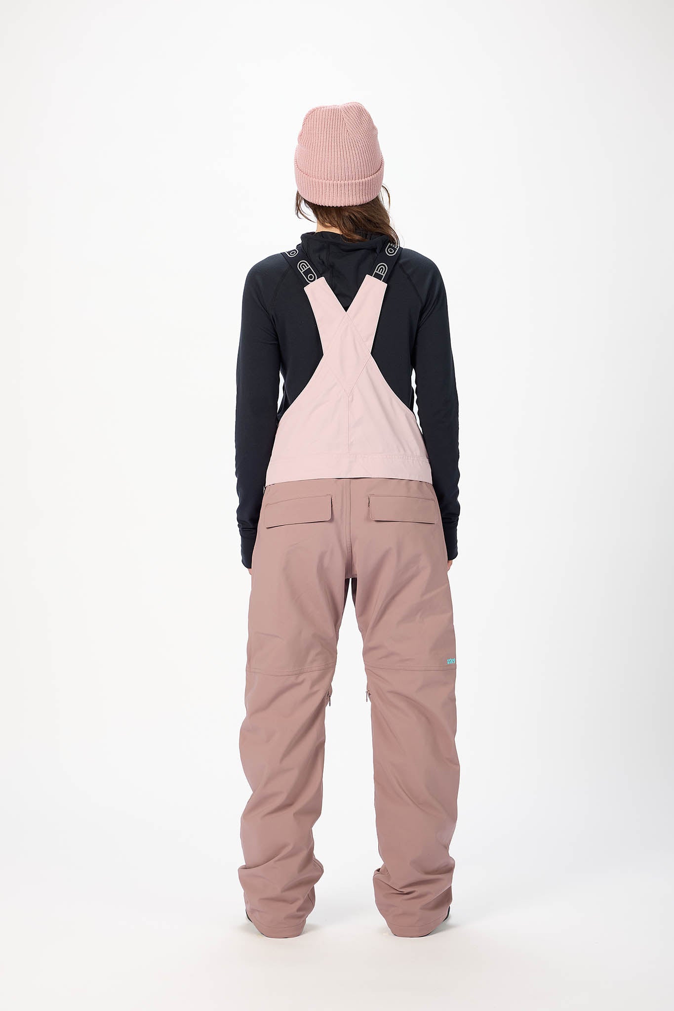 Person wearing a black jacket and pink overalls on a white background