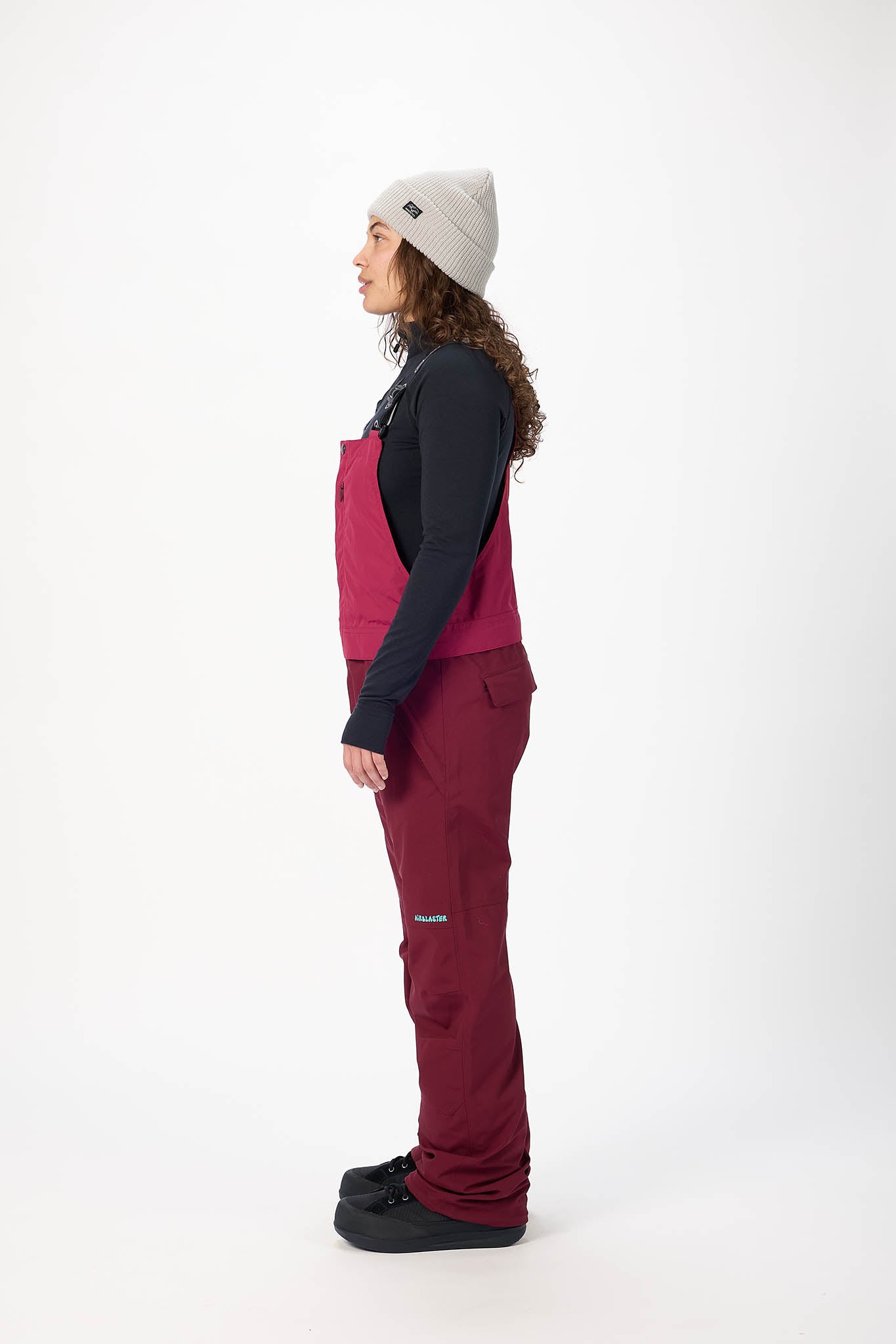 Person wearing a black jacket, pink vest, and maroon pants on a white background