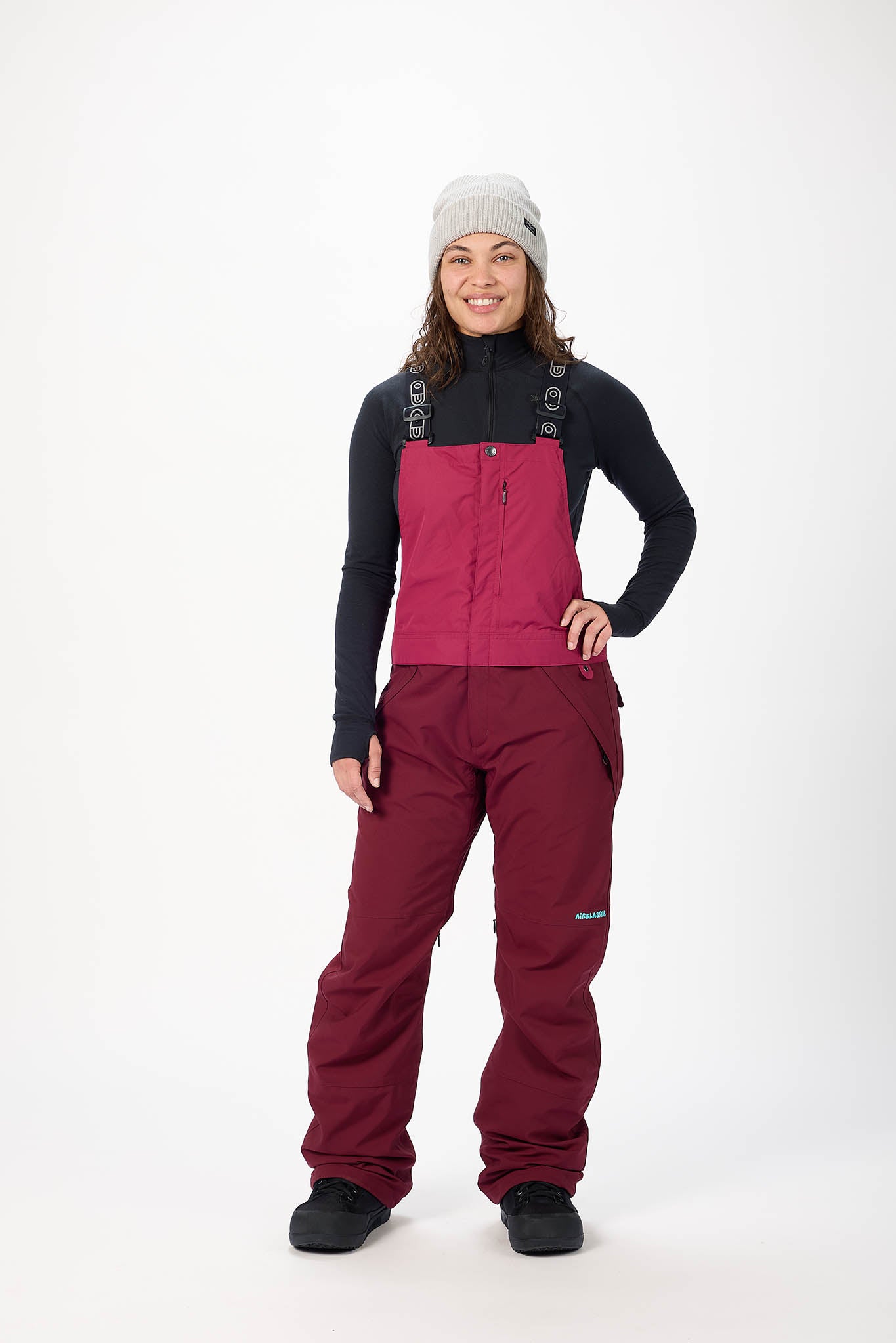Person wearing a black jacket and maroon snow pants on a white background