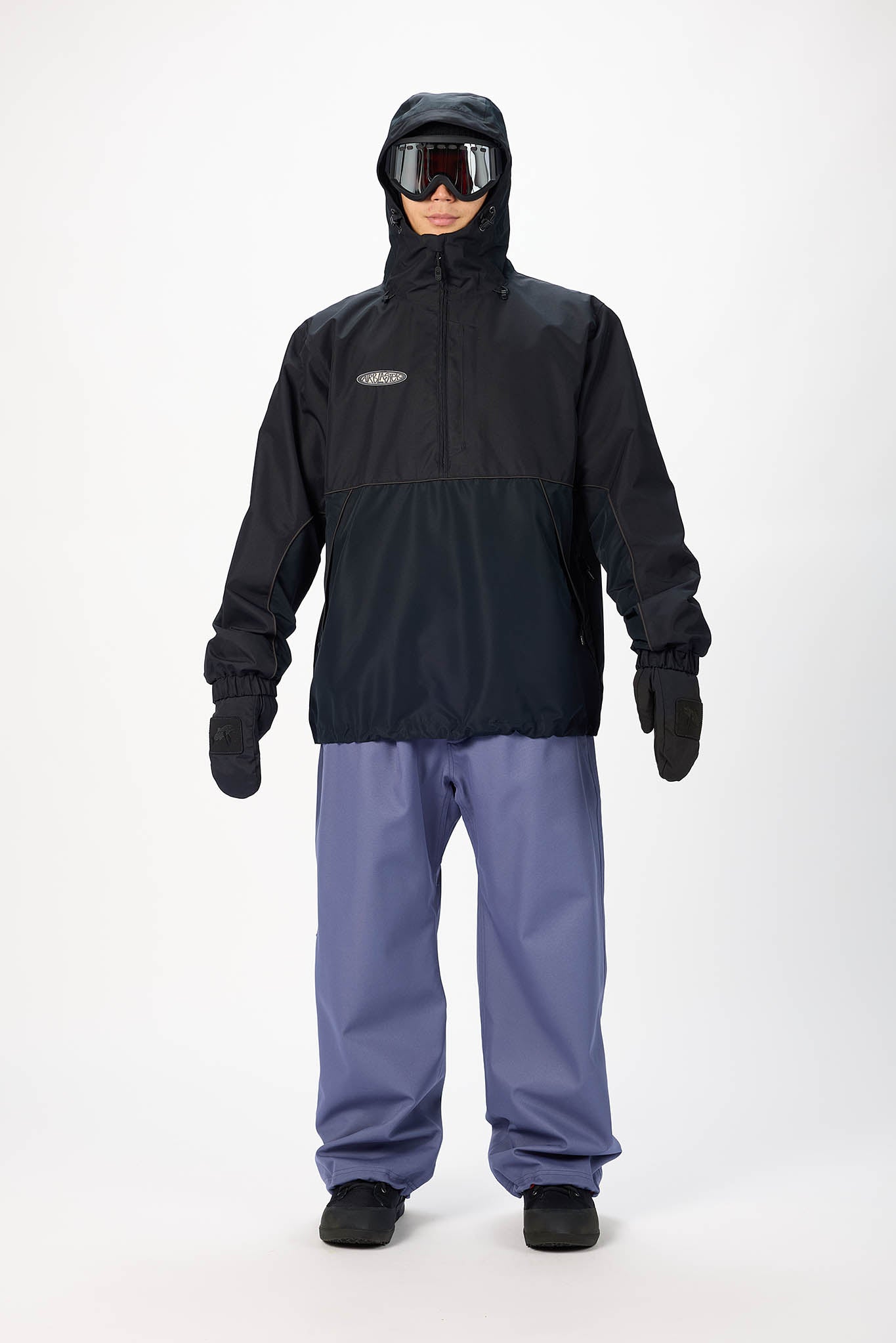 A model wearing a black hooded snow jacket with a small white logo on the chest, black gloves, and slate blue snow pants, standing against a plain white studio background.