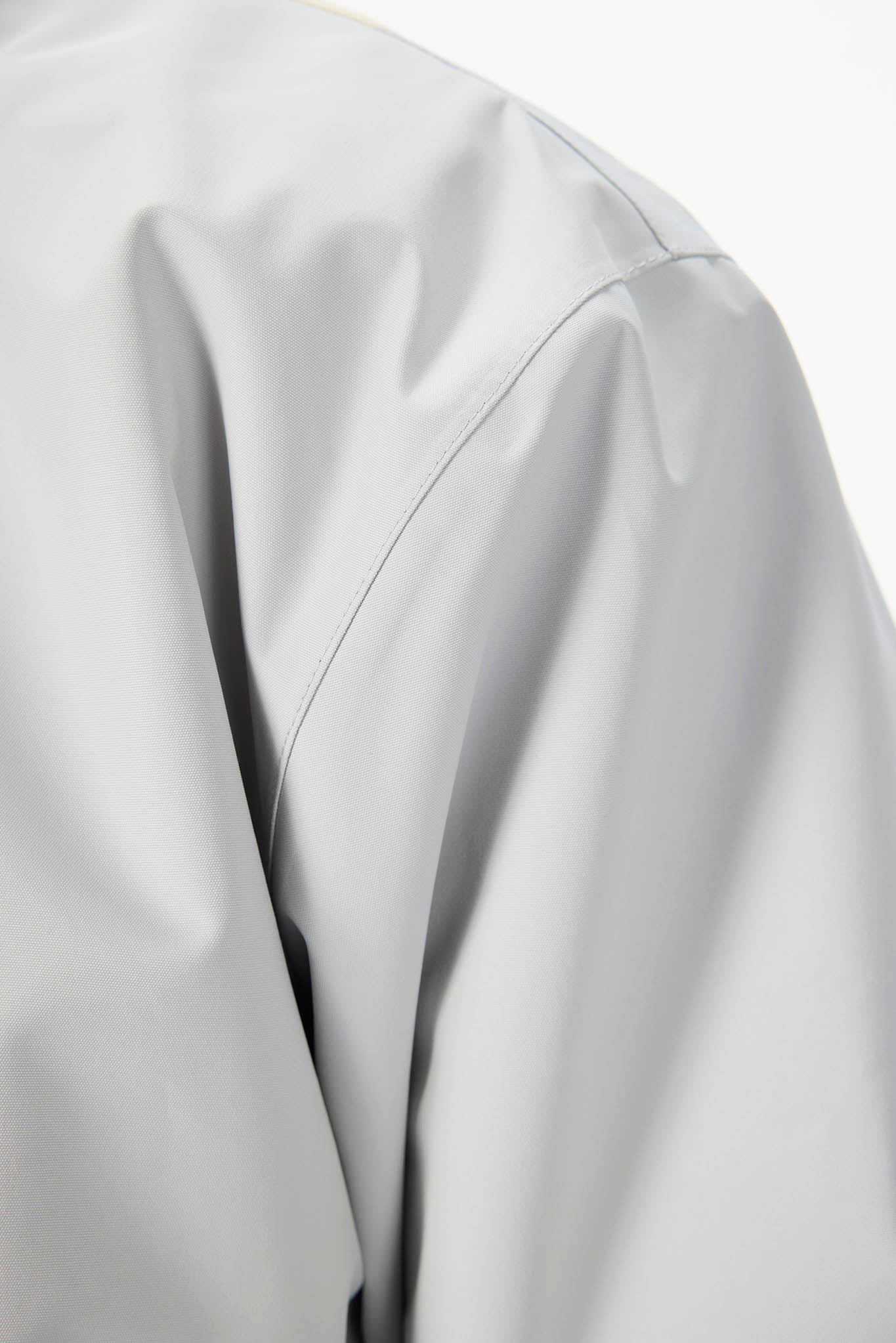 Close-up of a light gray jacket or fabric with a visible shoulder seam and smooth matte texture against a white background.