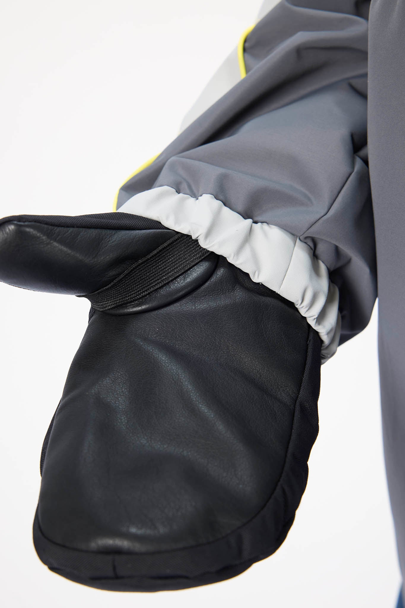 A close-up of a black leather-like mitten worn with a gray and white ski jacket, showing the cuff and elastic band.