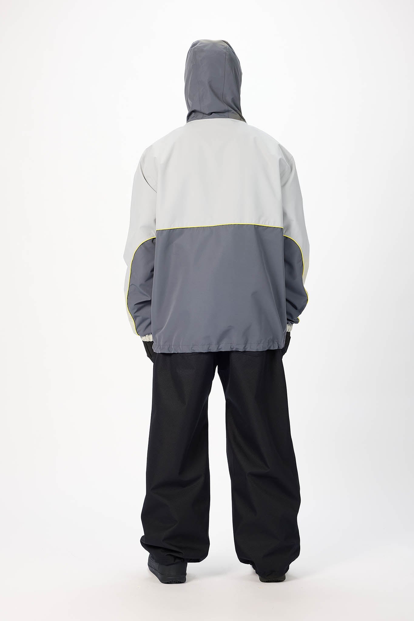 A person shown from the back wearing a colorblock hooded jacket with a light gray upper section, dark gray lower section, and black pants, photographed against a plain white studio background.