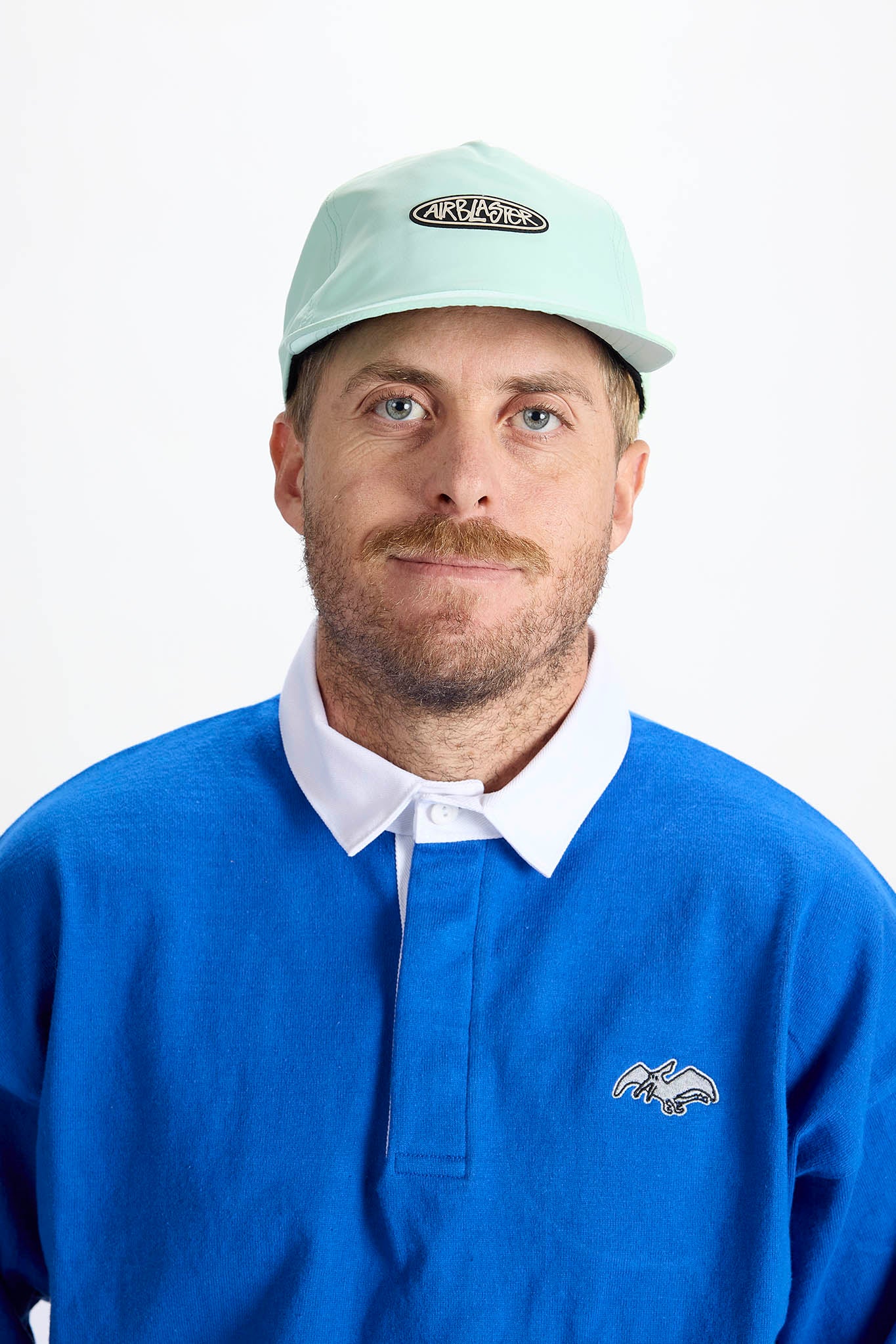 A man wearing a light mint green baseball cap with a black and white logo against a plain white background.