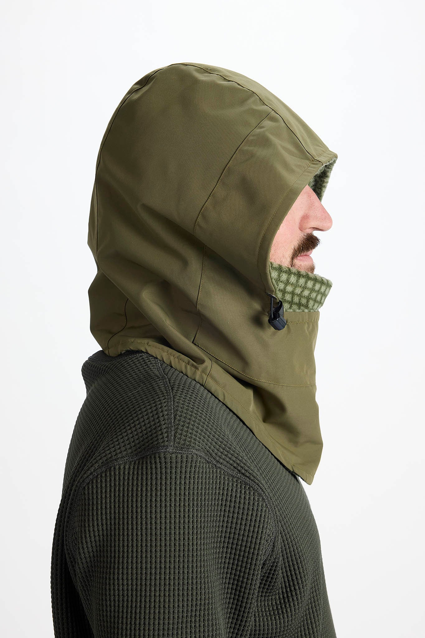 Side profile of a man wearing an olive green hooded balaclava face covering