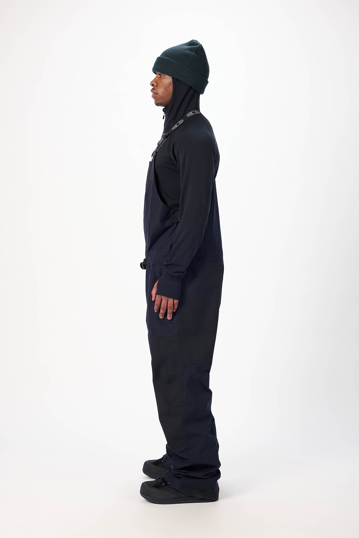 Person wearing a black snowmobile suit and green beanie on a white background
