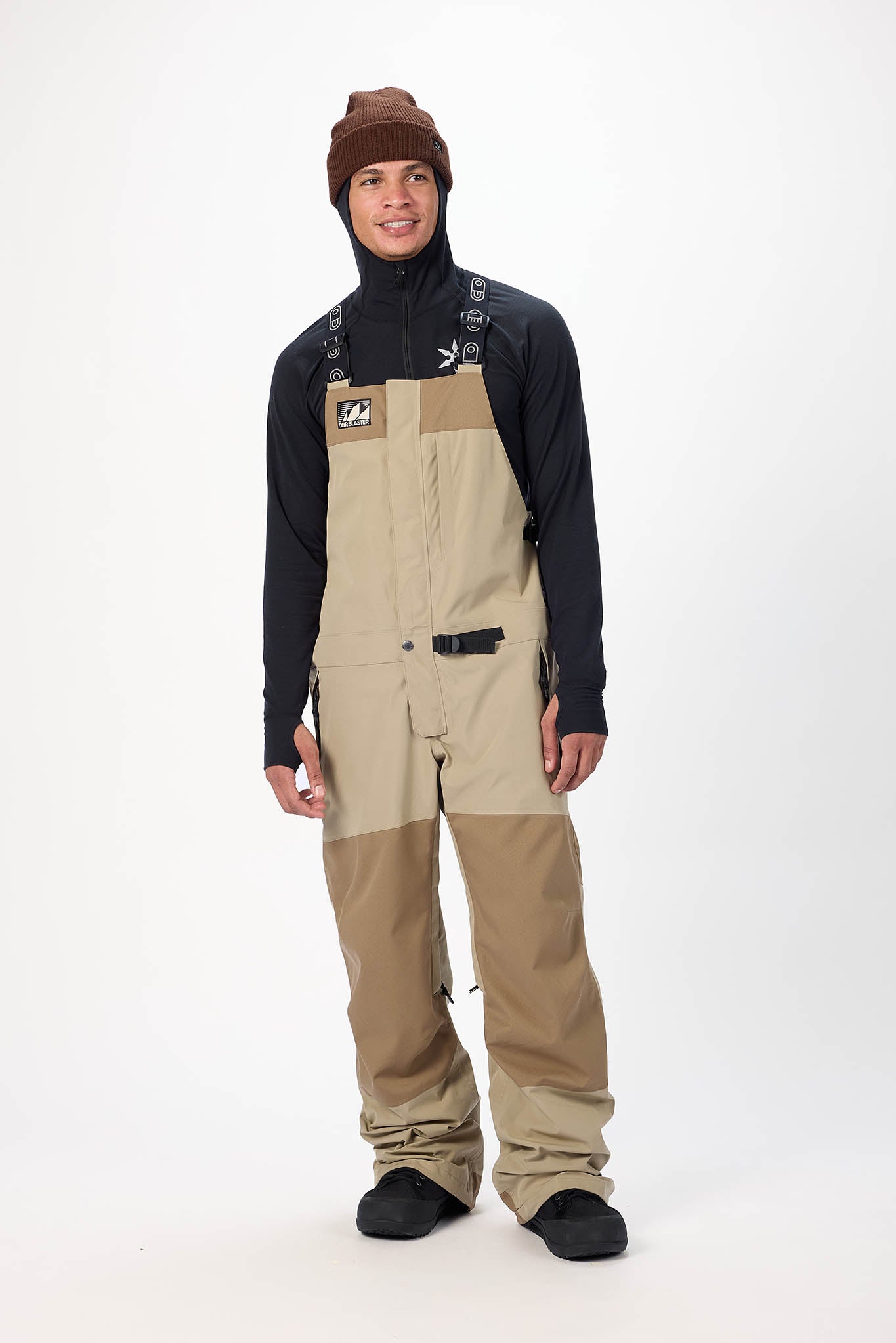 Person wearing a black jacket, brown beanie, and beige snow pants on a white background