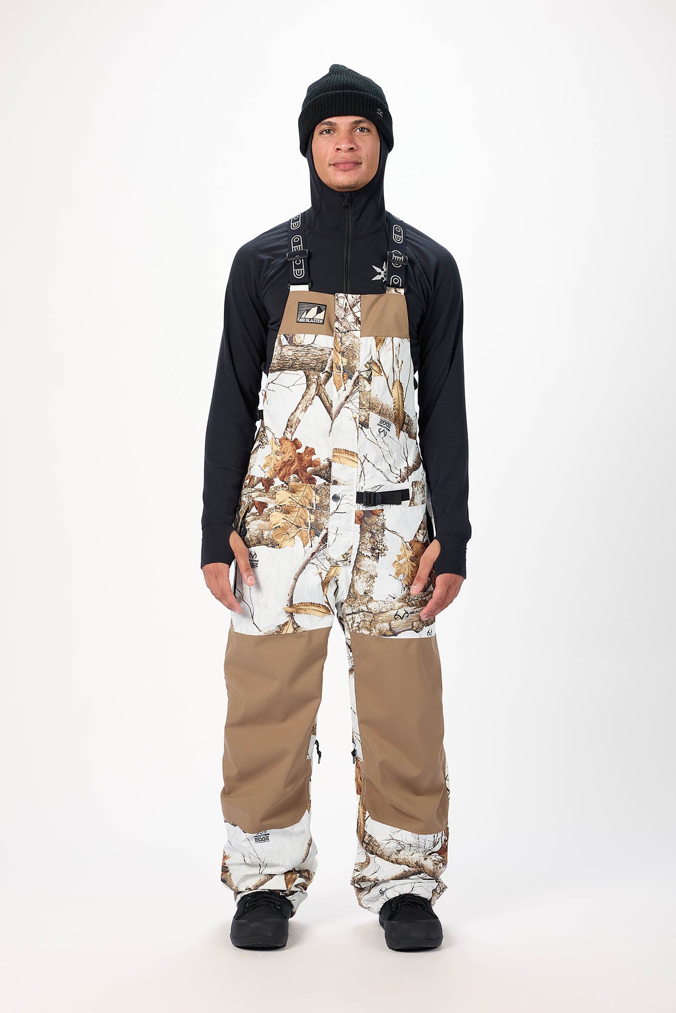 Person wearing a black jacket, black beanie, and camouflage overalls on a white background
