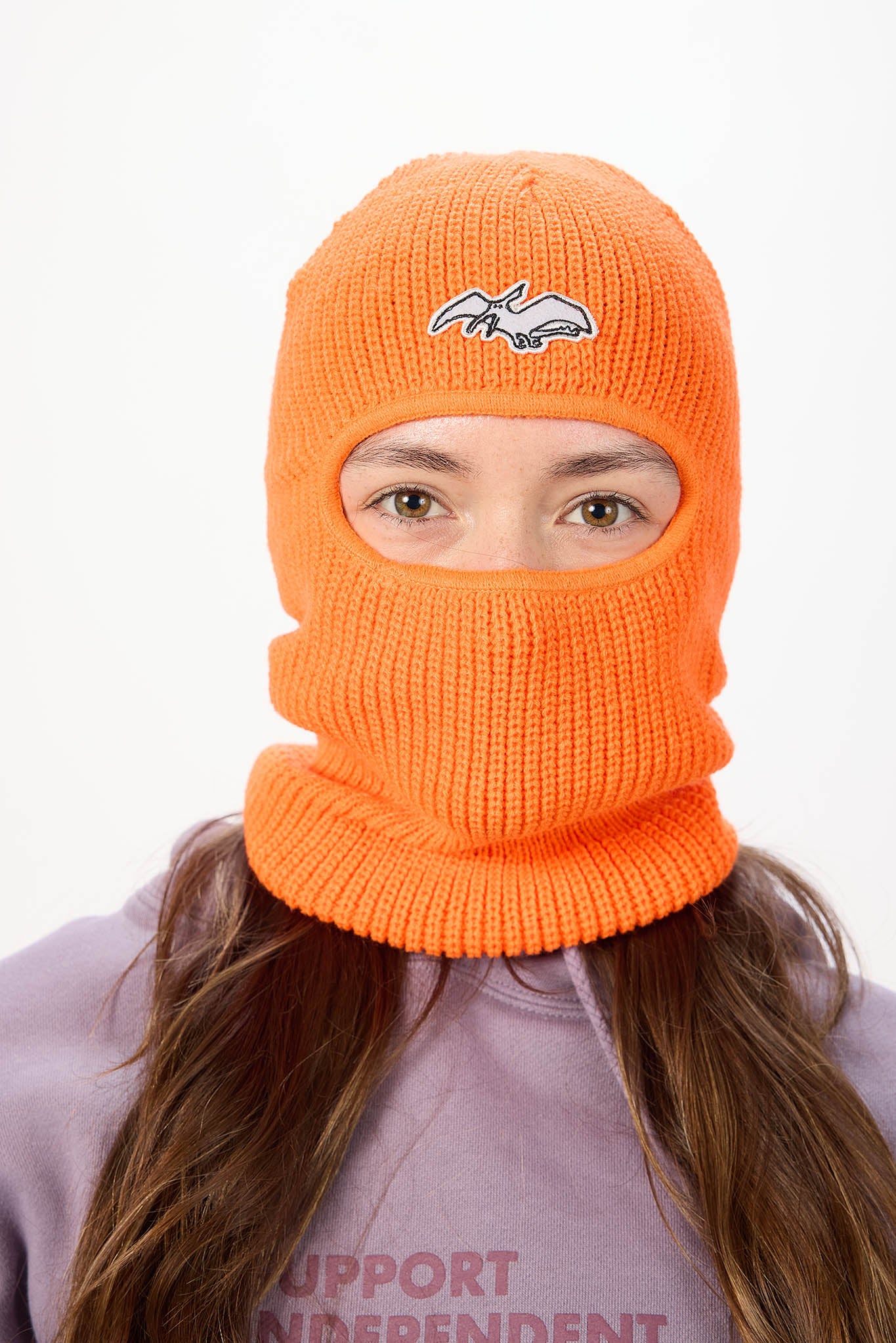 A person wearing a bright orange knit balaclava mask with a small white and gray terry logo on the forehead, shown against a plain white background.