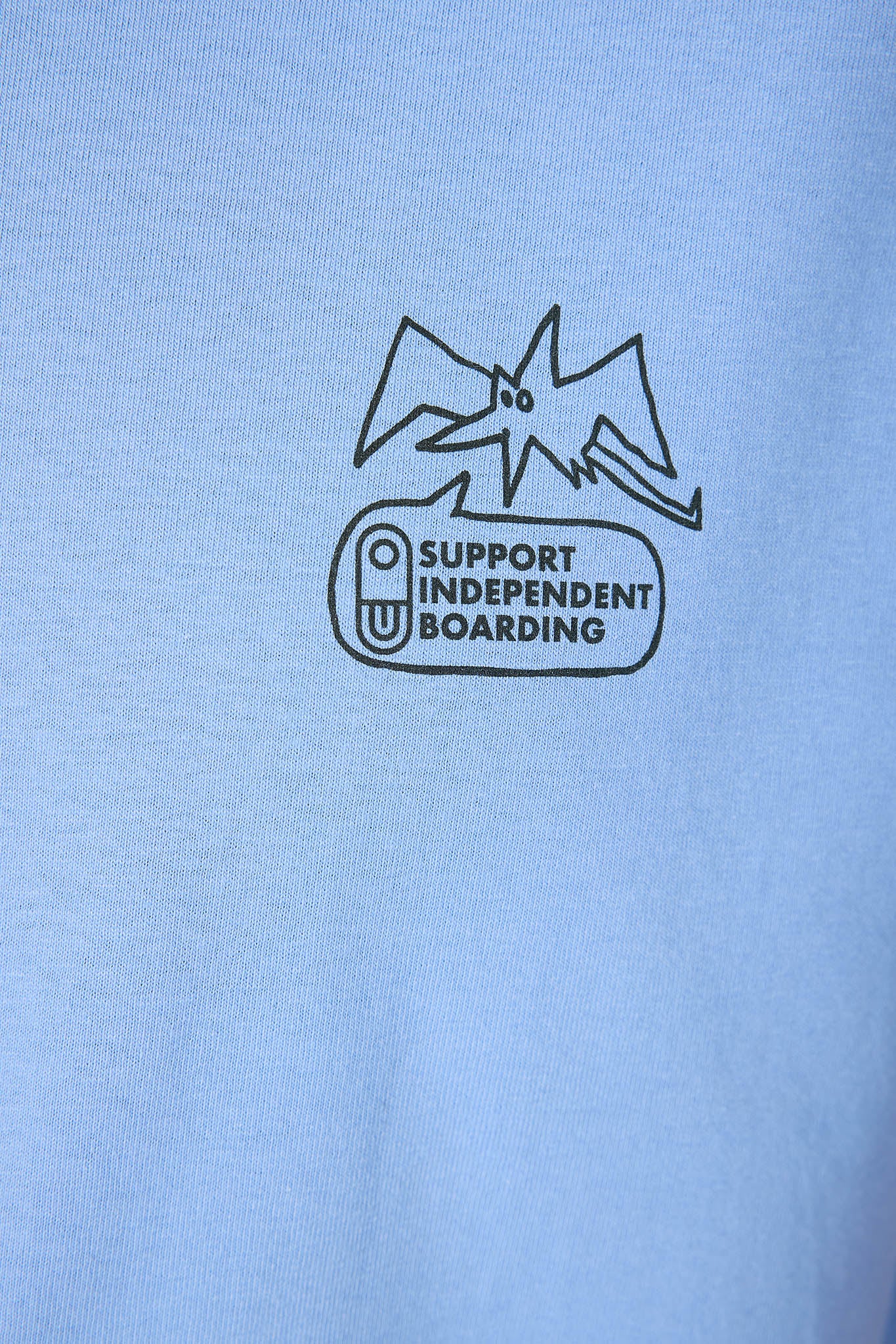 A close-up of a light blue t-shirt featuring a black graphic print of a bat above a speech bubble that reads 'SUPPORT INDEPENDENT BOARDING'.