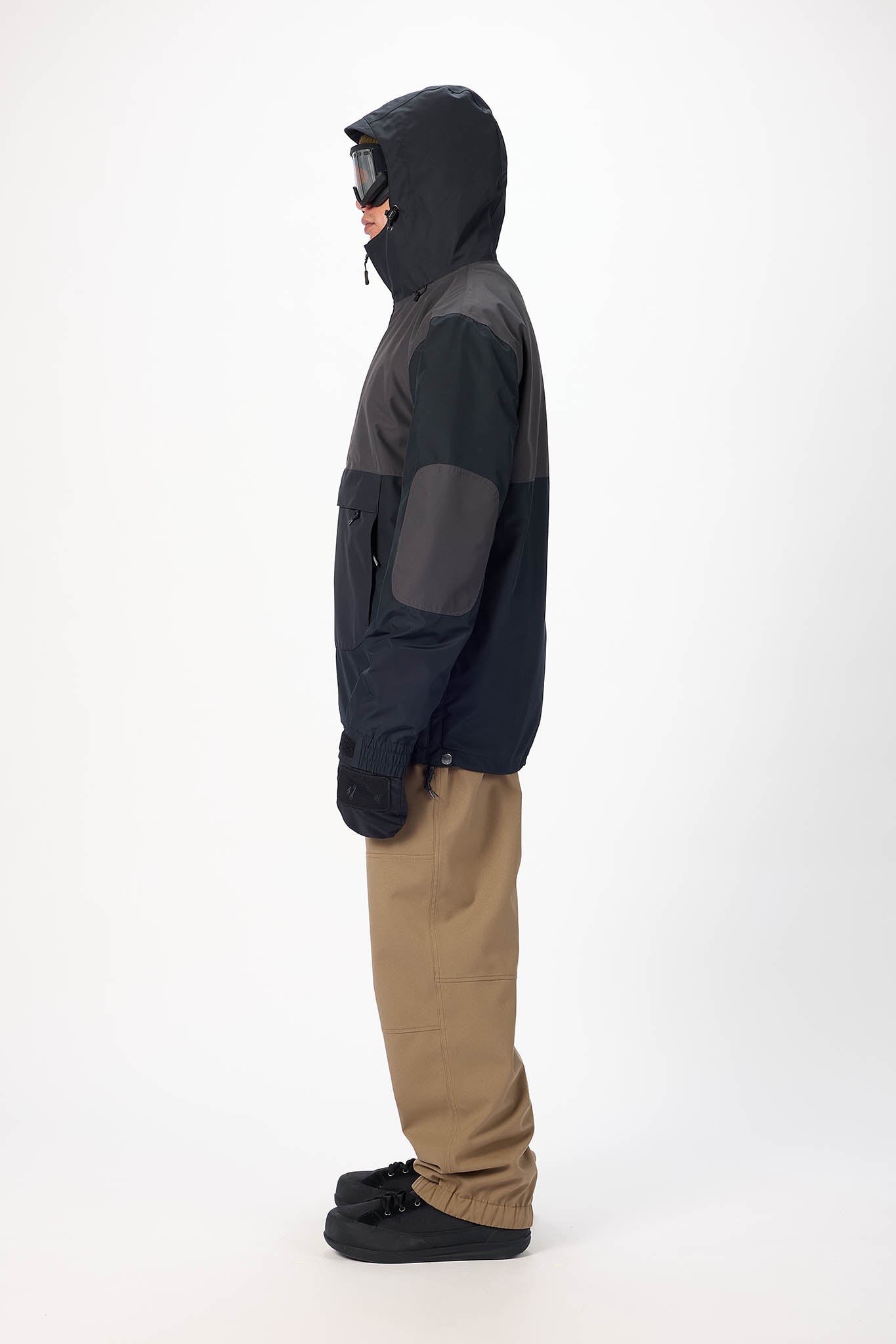 Person wearing a black jacket and tan pants on a white background