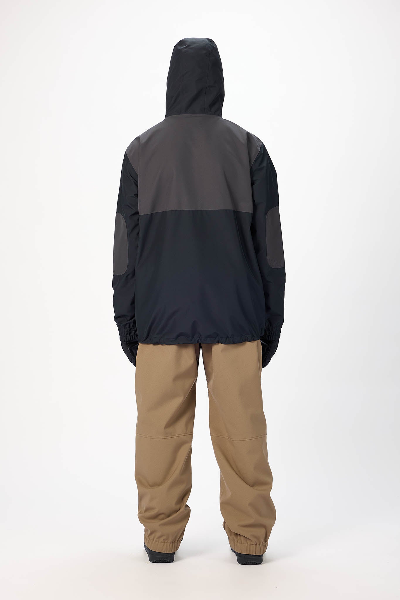 Person wearing a black and gray jacket with beige pants on a white background