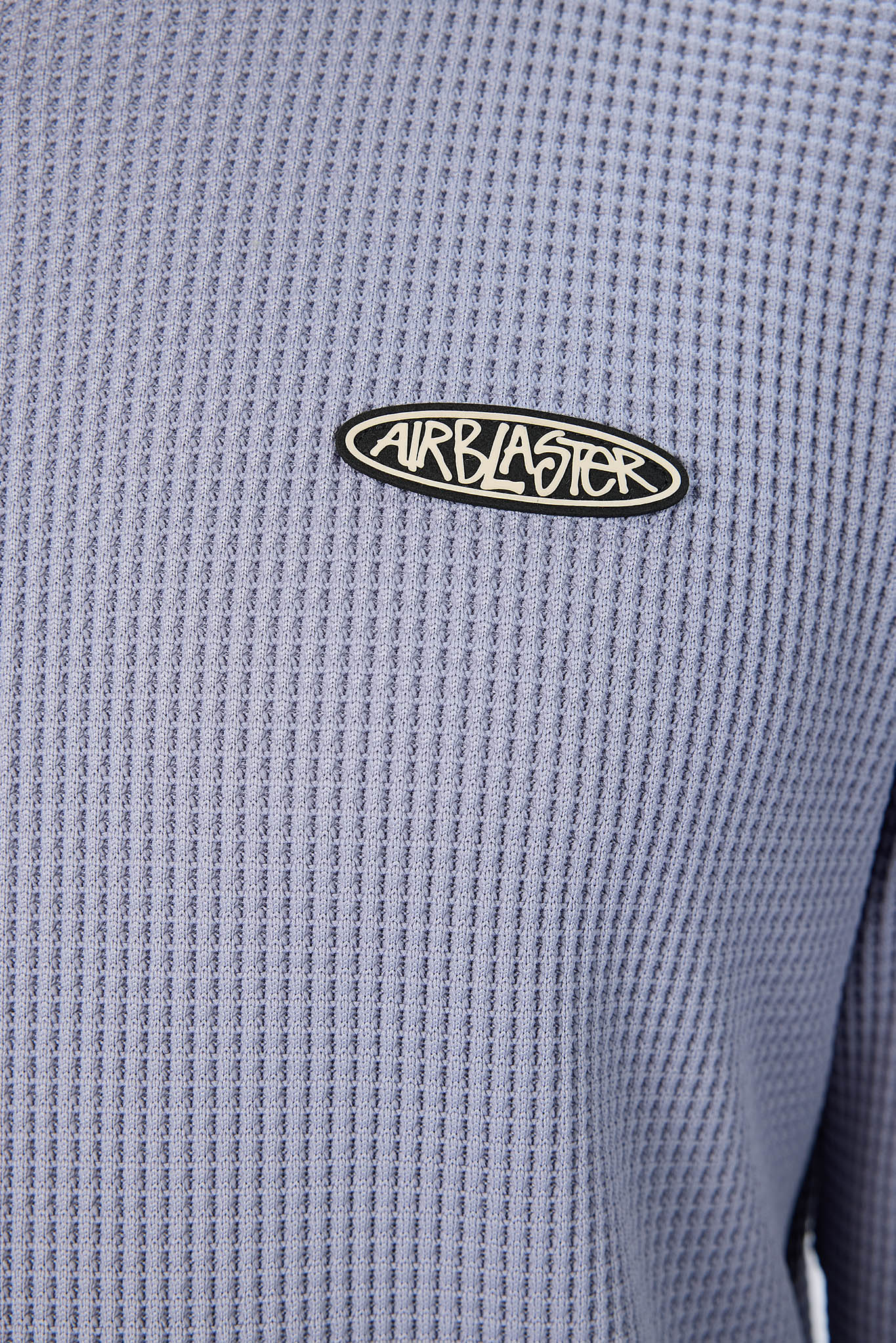 Close-up of a textured light blue-gray waffle knit top with an oval black and white Airblaster logo patch on the chest.