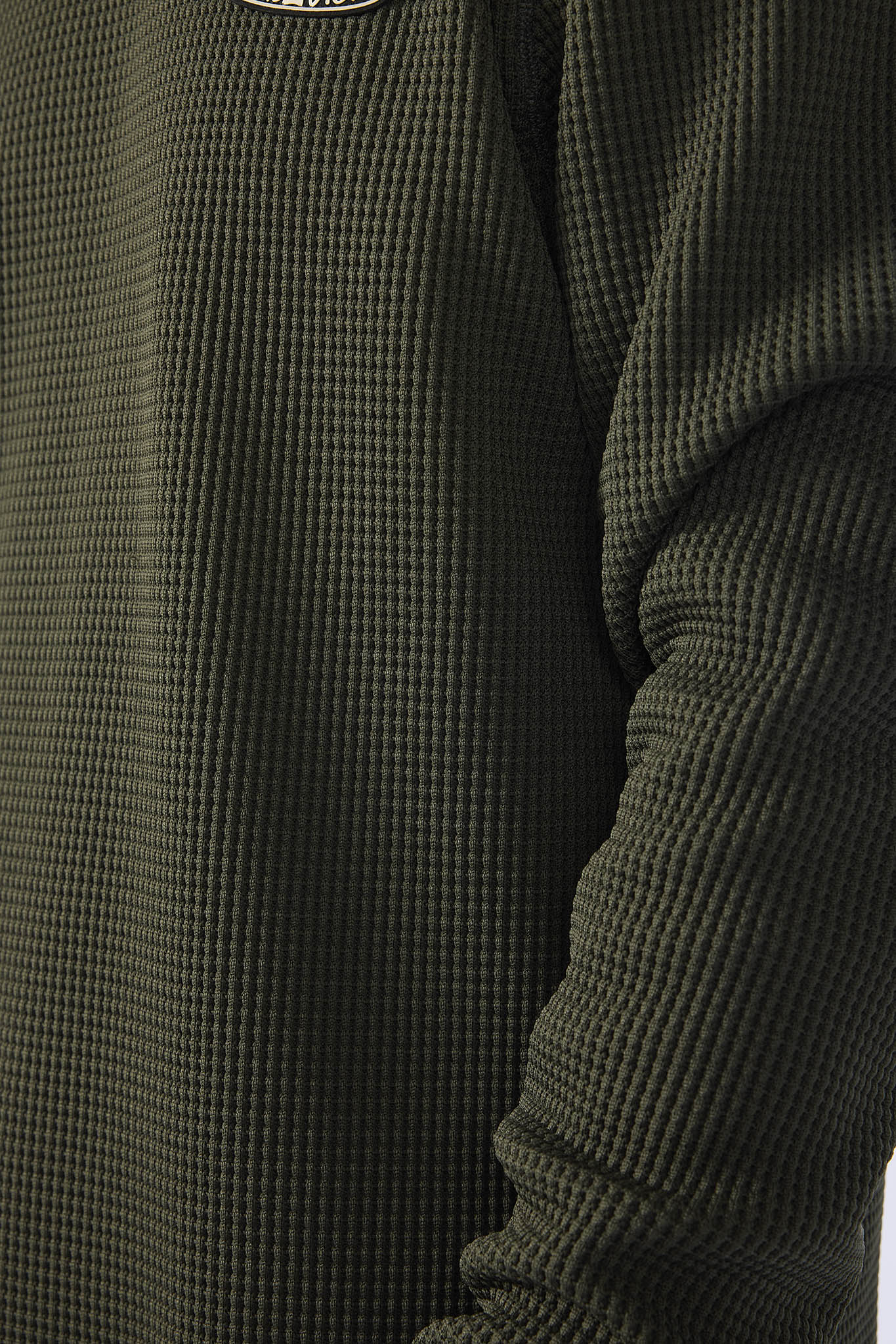 Close-up of a dark olive green waffle-knit long-sleeve top, showing the textured fabric and ribbed sleeve.