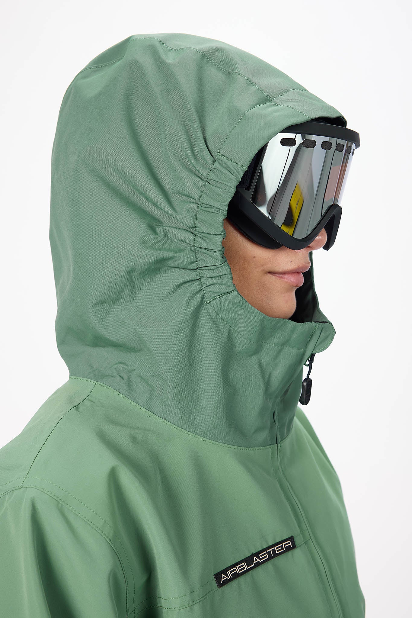 Person wearing a green hooded jacket with goggles on a white background