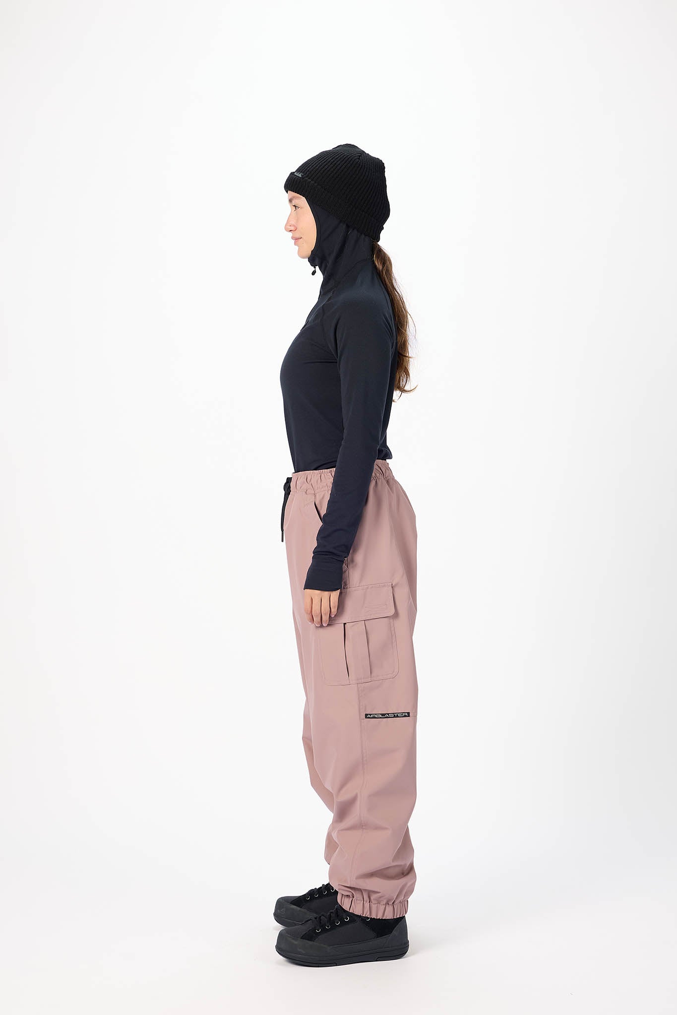 Person wearing a dark hoodie and light pink cargo pants on a white background